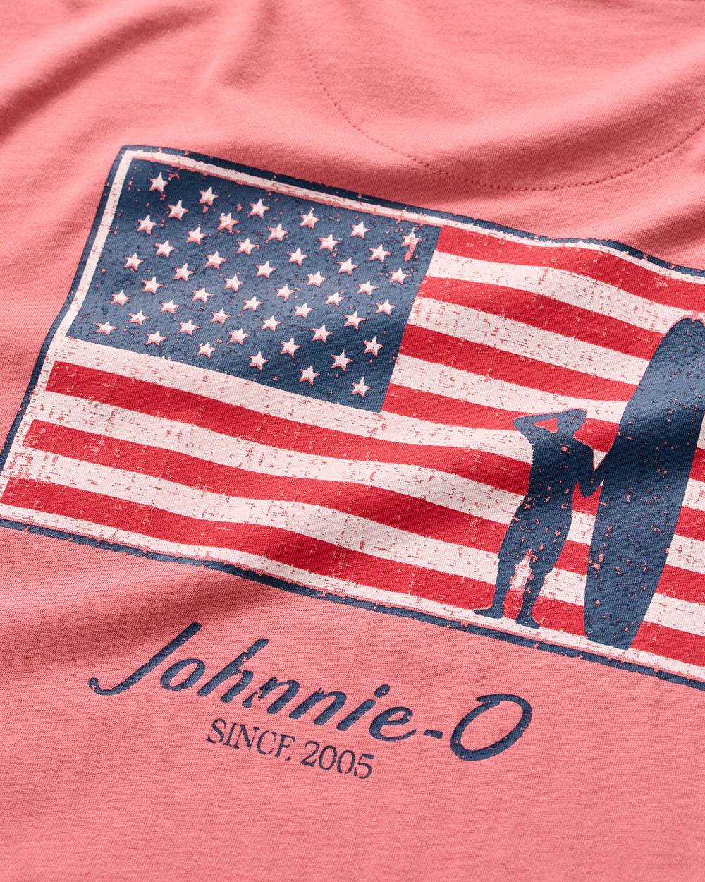 The Johnnie-O "American Dream" pink short sleeve tee features a vintage-style American flag graphic with a surfer and “Johnnie-O SINCE 2005” text above the pocket.