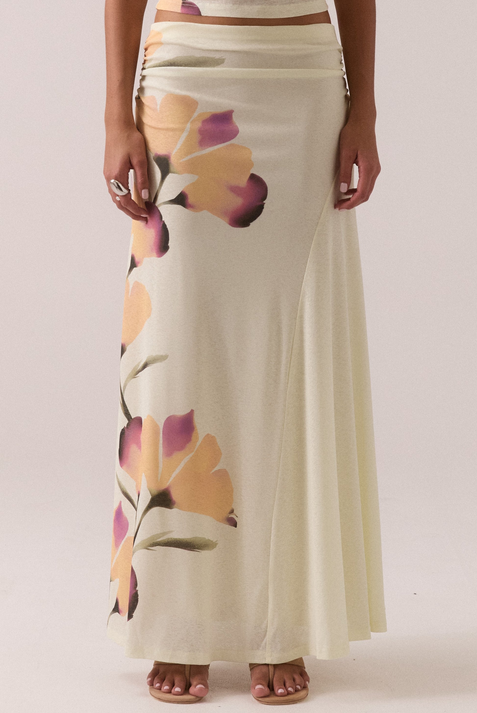 A person models the Sovere Akanni Skirt in Yellow Multi, featuring a long mesh design with large soft florals, standing barefoot against a plain background.