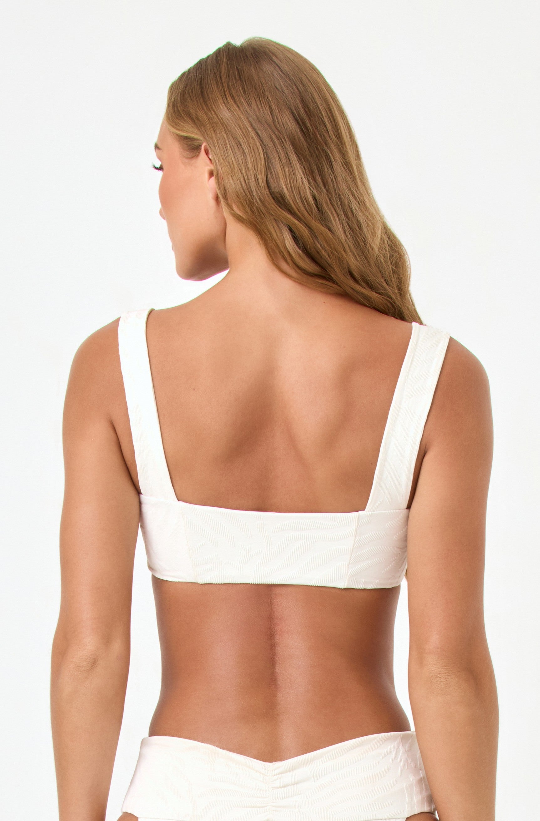 A woman with long, light brown hair is shown from the back wearing the LSpace Sail Along Stripe Marlee Top, a bralette style swimsuit, against a plain white background.