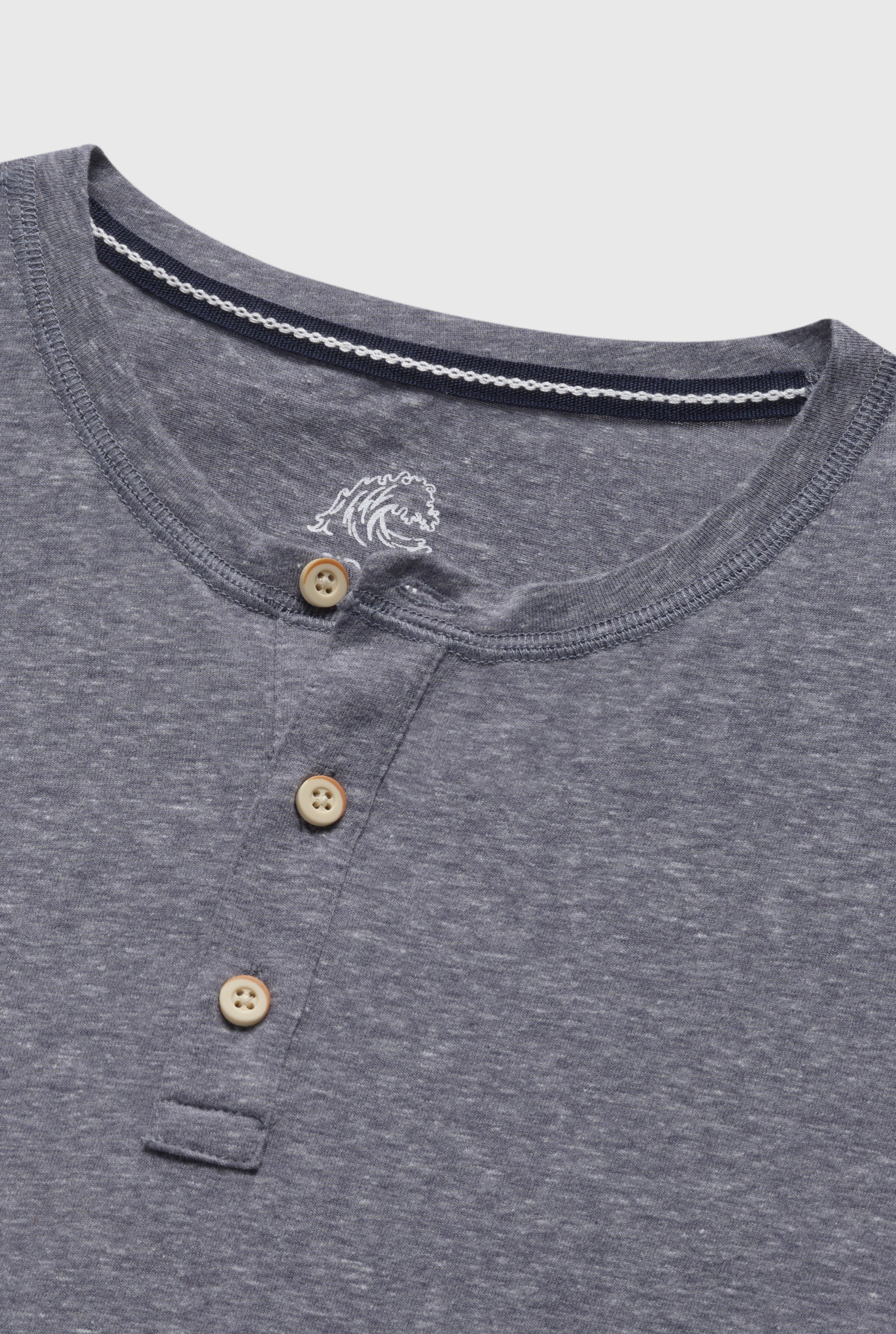 Close-up of the Surfside Supply Co. Sean Short Sleeve Single Dye Jersey Henley in heathered gray, regular fit, featuring three tan buttons and a small white embroidered lion’s head near the neckline.