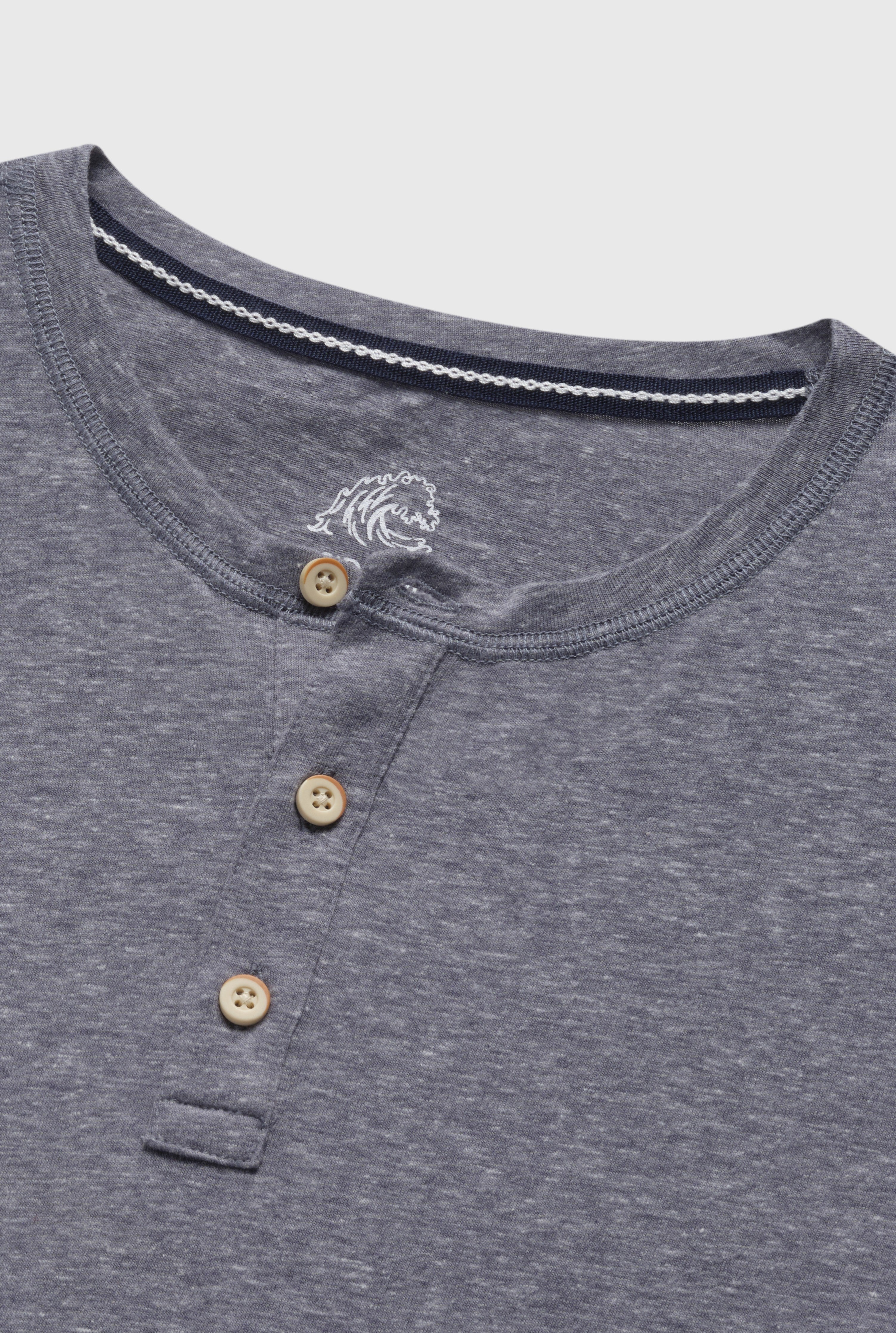 Close-up of the Surfside Supply Co. Sean Short Sleeve Single Dye Jersey Henley in heathered gray, regular fit, featuring three tan buttons and a small white embroidered lion’s head near the neckline.