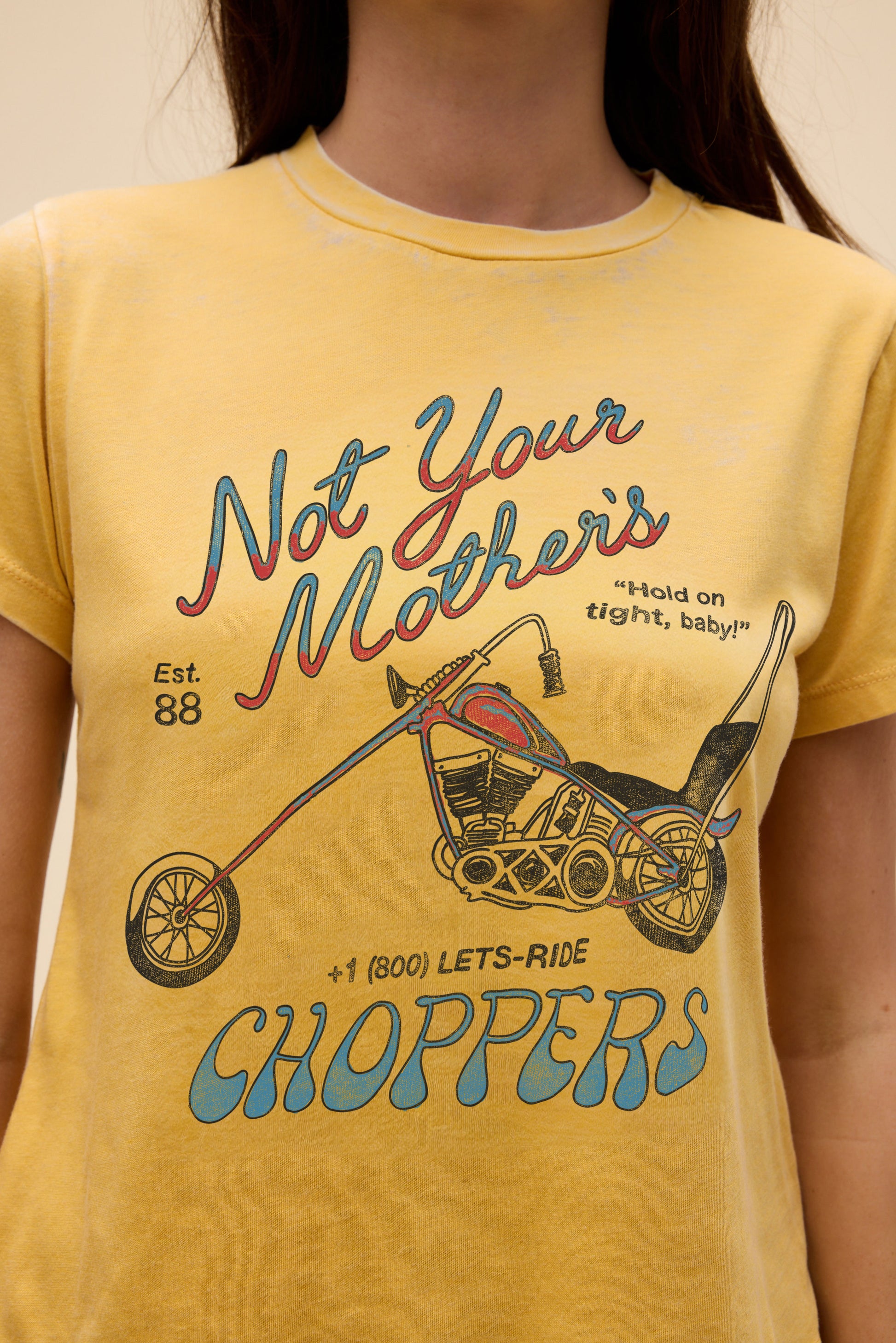 Someone wears the Daydreamer LA Not Your Mothers Choppers yellow tee, featuring a graphic chopper motorcycle and the slogans “Not Your Mother’s Choppers,” “Hold on tight, baby!!”, and “+1 (800) LETS-RIDE” on soft burnout jersey.