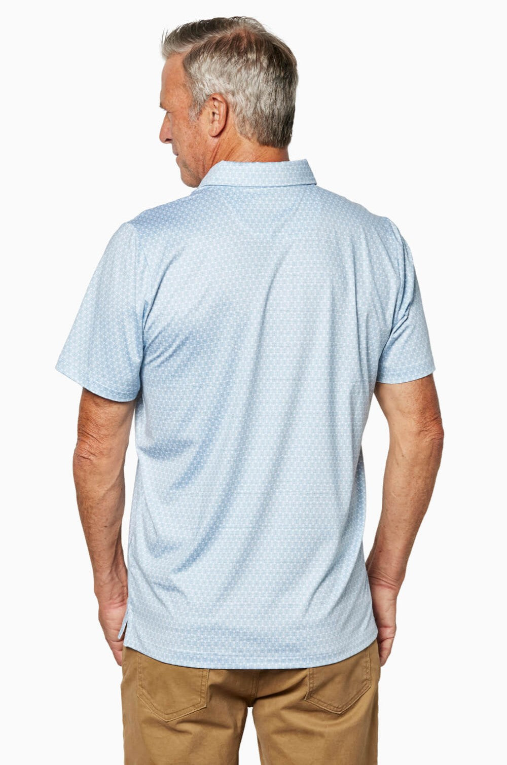 A man with gray hair is seen from behind wearing the Toes on the Nose Clubhouse Polo Tequila Therapy, a light blue, short-sleeved collared shirt with a subtle pattern and quick-dry fabric, paired with tan pants against a white background.