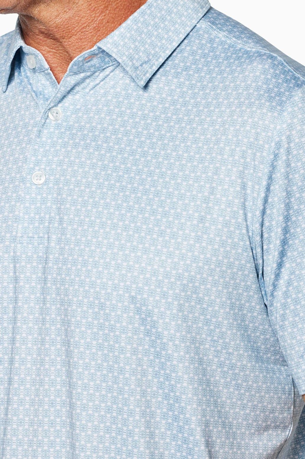 A close-up of a man's chest and shoulder wearing the Toes on the Nose Clubhouse Polo Tequila Therapy—a light blue, short-sleeved, collared button-up with subtle geometric pattern and moisture-wicking, quick-dry fabric. The man’s face is not visible.