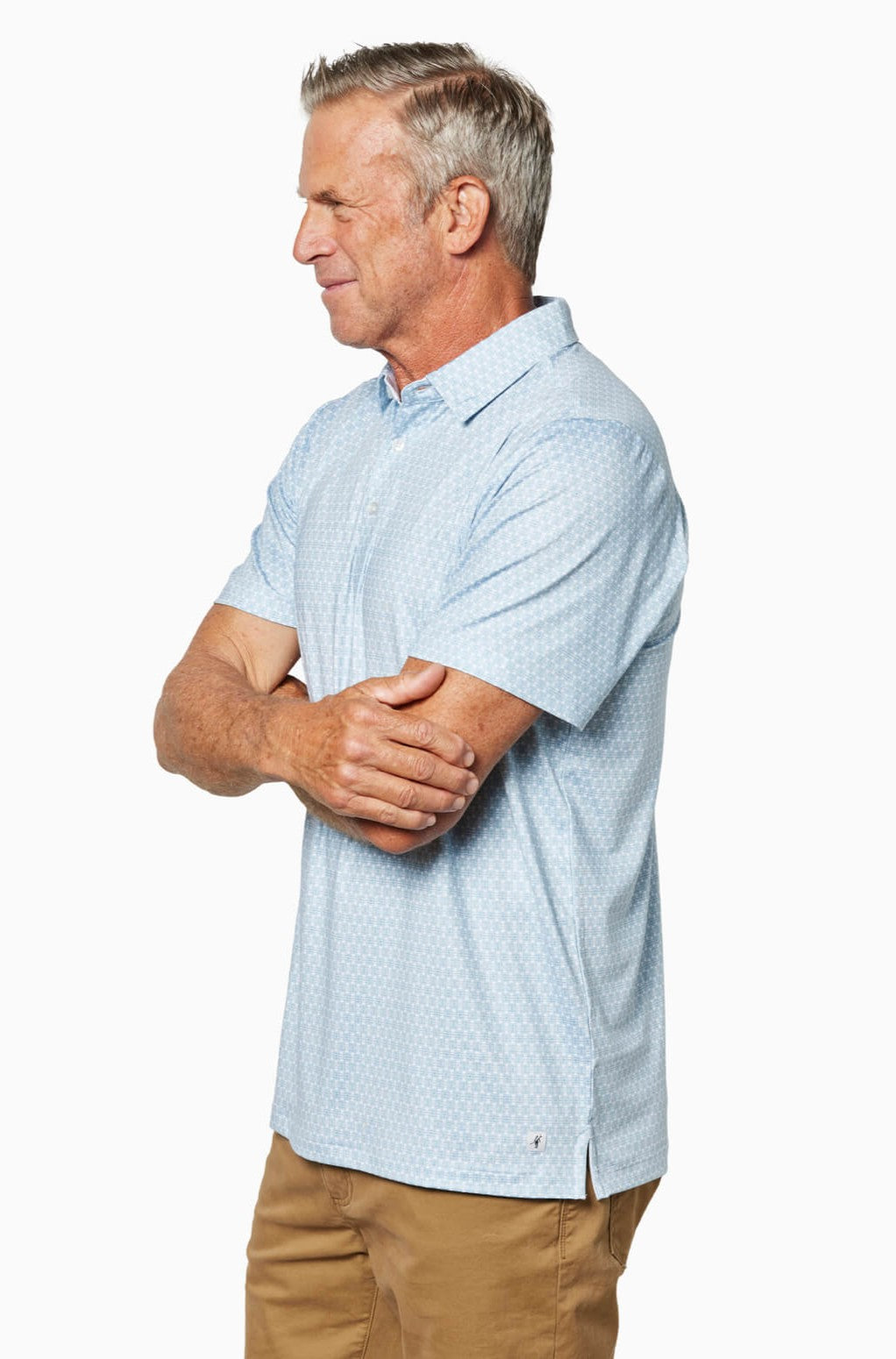 Older man with gray hair stands in profile, arms crossed, wearing the Toes on the Nose Clubhouse Polo Tequila Therapy shirt and tan pants, against a white background.