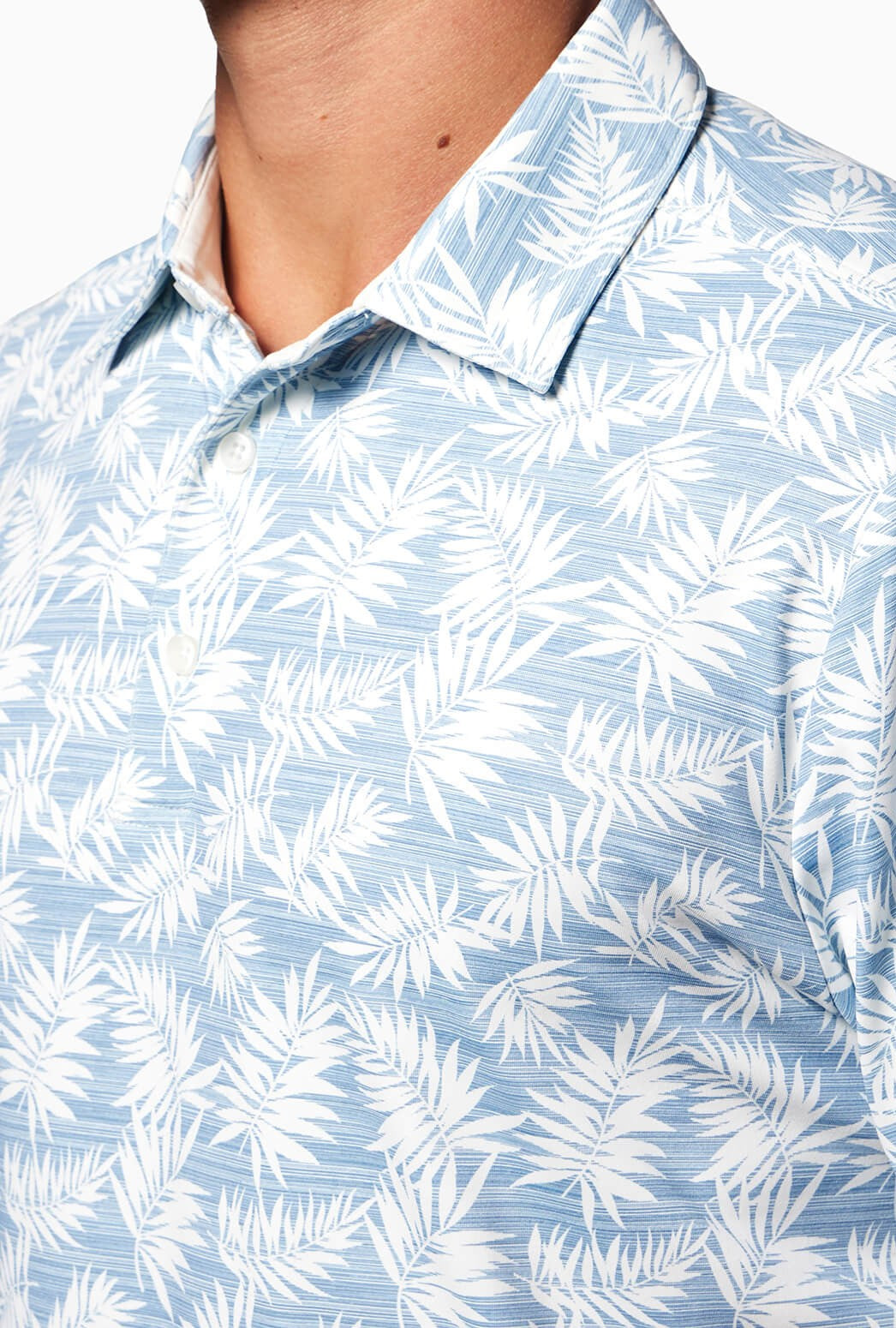 A person wearing the Toes on the Nose Clubhouse S/s Polo in light blue with a white tropical leaf pattern, shown from shoulders to mid-chest with only the lower face partially visible. This quick-dry, moisture-wicking shirt is comfortable and stylish.