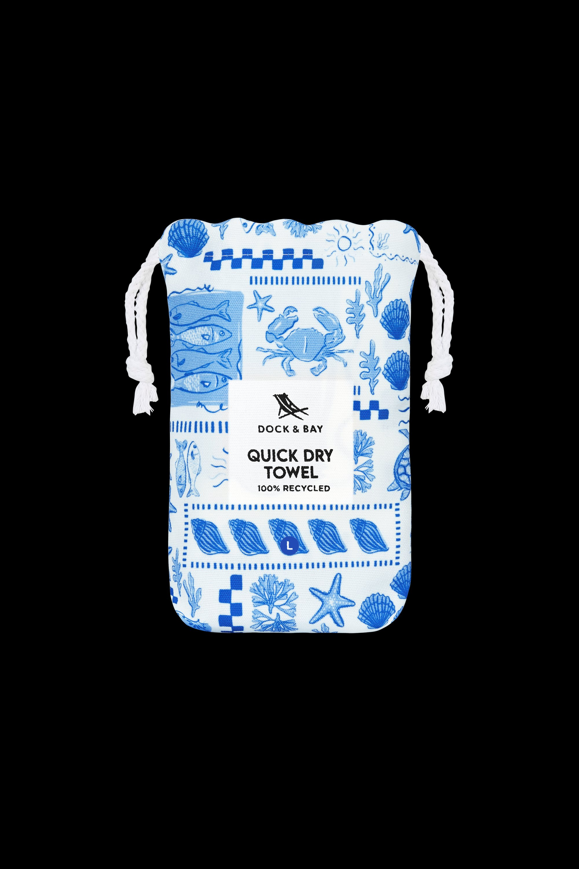 A lightweight drawstring bag features blue sea-inspired illustrations—shells, fish, and crabs—on white. The front label reads South Moon Under Grecian Shores Large Towel, known for its quick dry microfibre design and 100% recycled material.