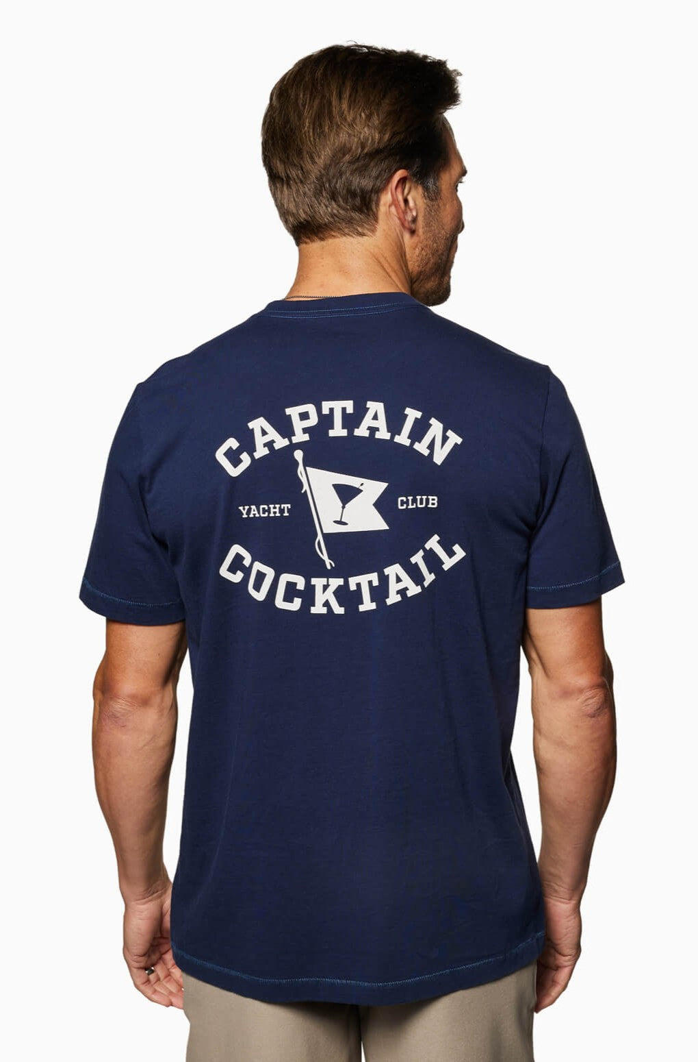 A man is seen from behind wearing the Toes on the Nose Yacht Club Short Sleeve Tee in navy blue, featuring white text that reads Captain Cocktail Yacht Club and a flag with a cocktail glass icon.