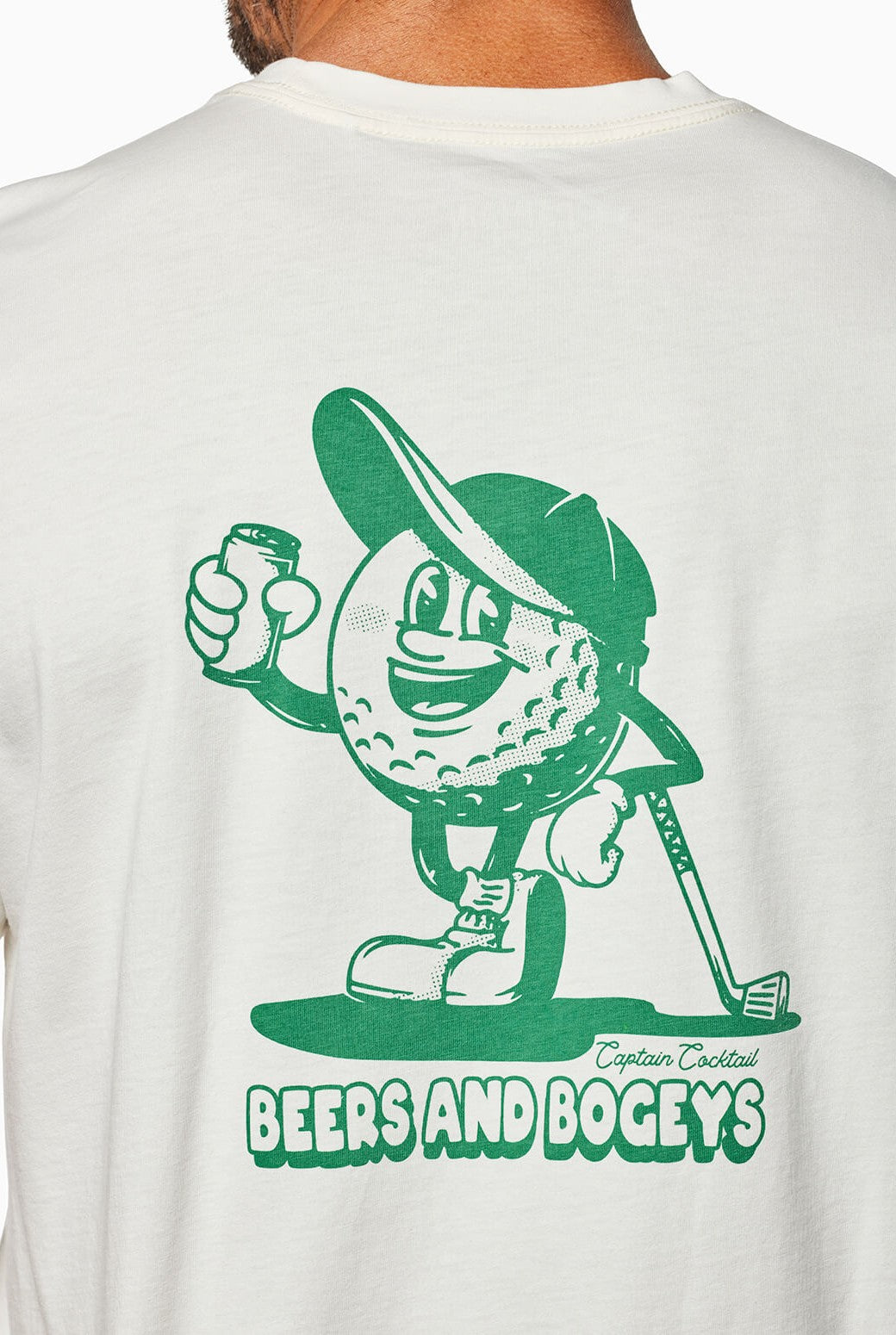 Wearing the Toes on the Nose Beers And Bogeys relaxed fit white shirt, made from premium Peruvian cotton, with a green cartoon golf ball holding a beer and golf club, plus text: BEERS AND BOGEYS and “Captain Cocktail.”.