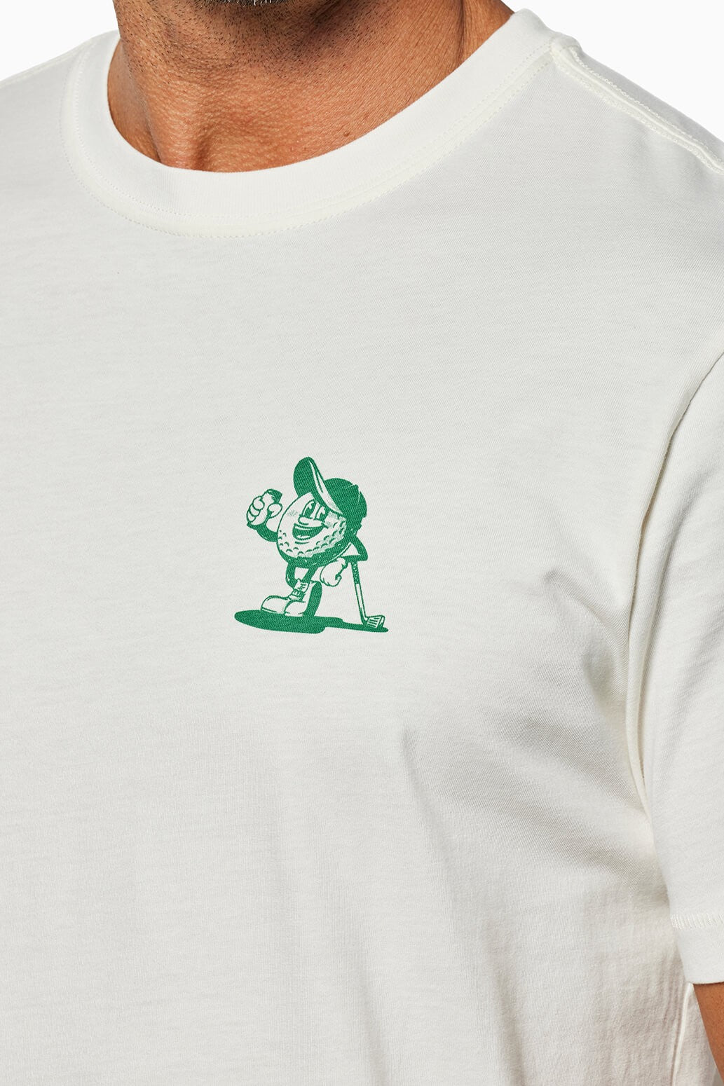 Close-up of a person wearing the “Beers And Bogeys” relaxed fit white T-shirt by Toes on the Nose, made from premium Peruvian cotton, with a small green cartoon baseball—Captain Cocktail with bat—on the left chest.