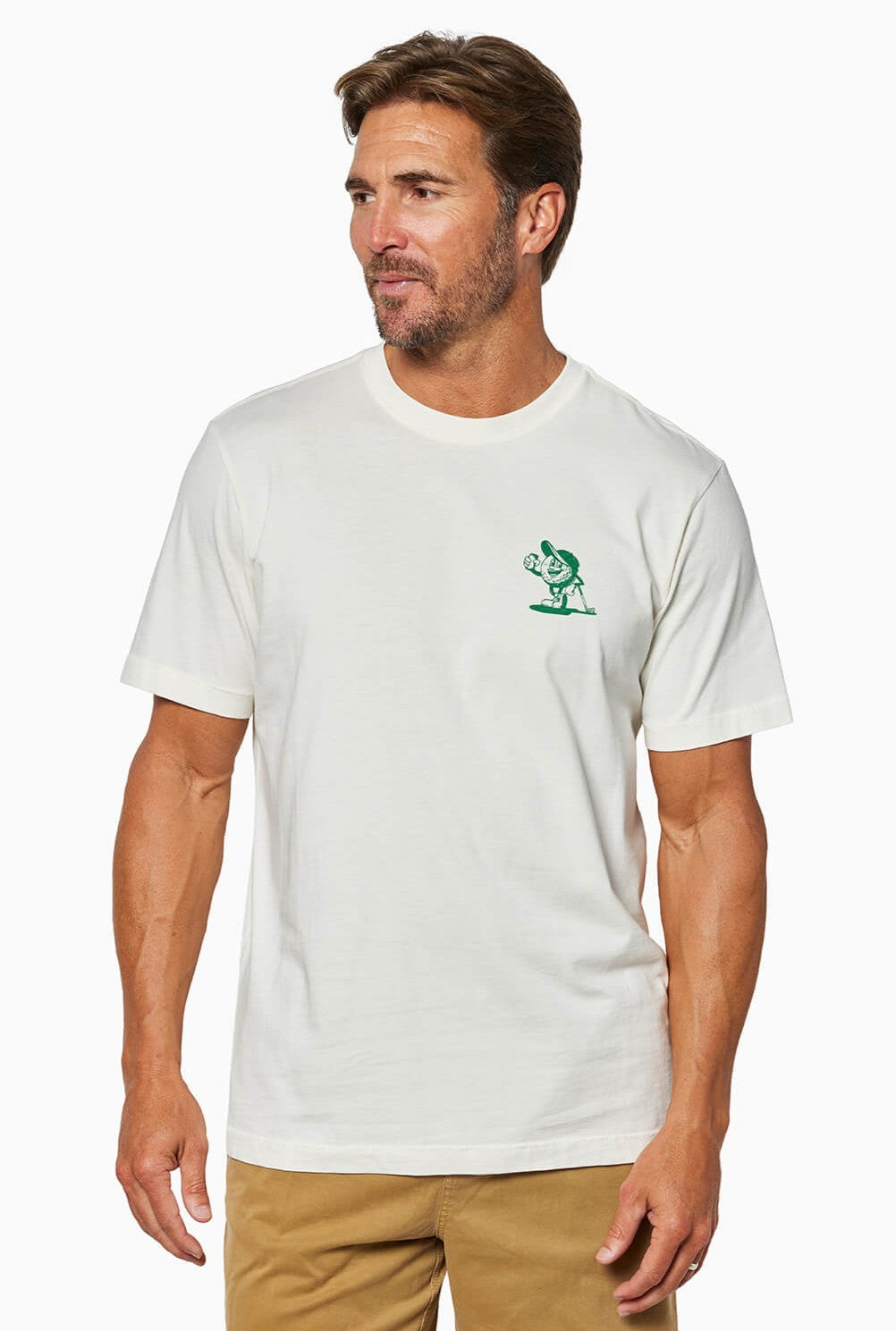 A man stands against a white background wearing the Toes on the Nose "Beers And Bogeys" relaxed fit white t-shirt with a green cartoon graphic on the left chest and khaki pants, made from premium Peruvian cotton.