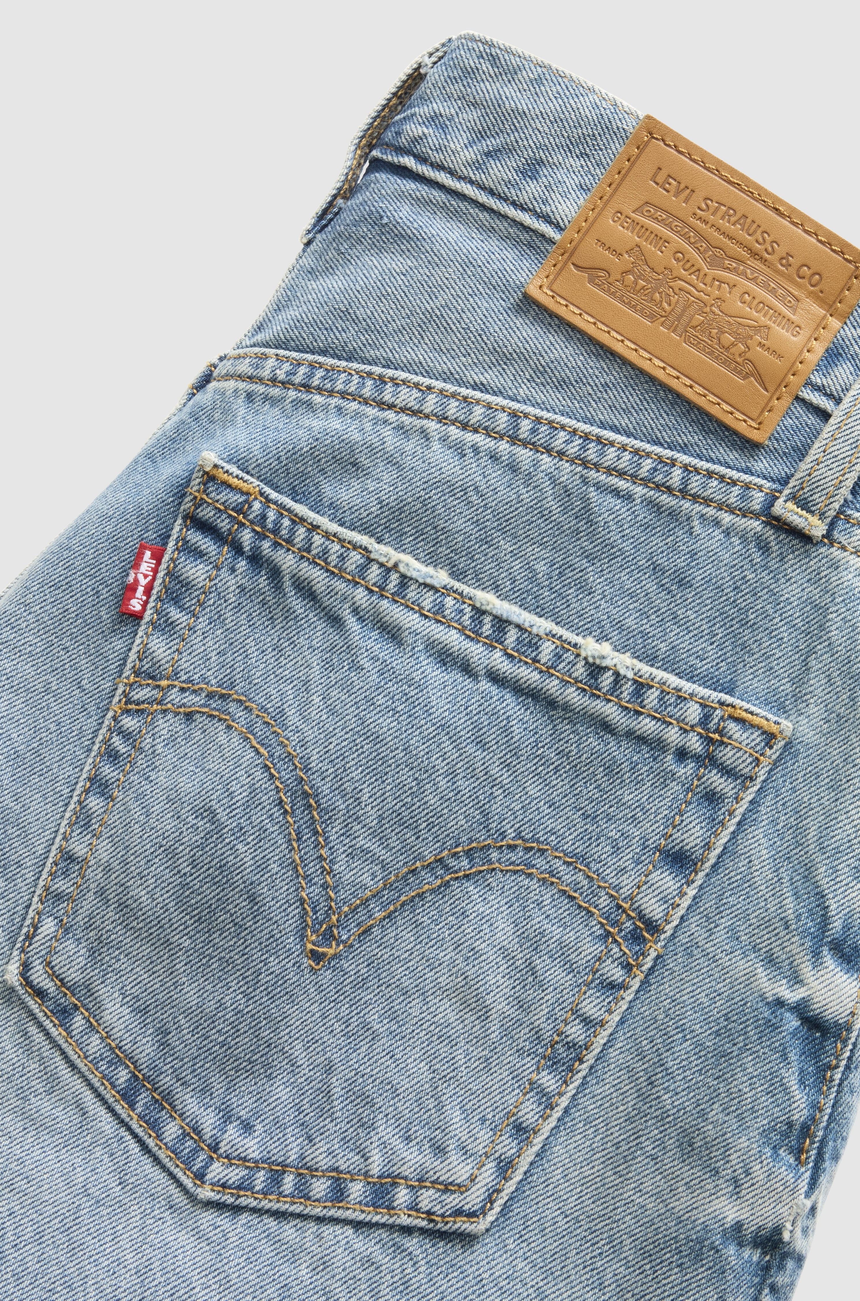 Close-up of the back pocket and waistband of Levi’s Ribcage Short Zip Blow My Mind in light blue, showcasing the signature leather patch, red tab, yellow stitching, and 100% cotton denim.