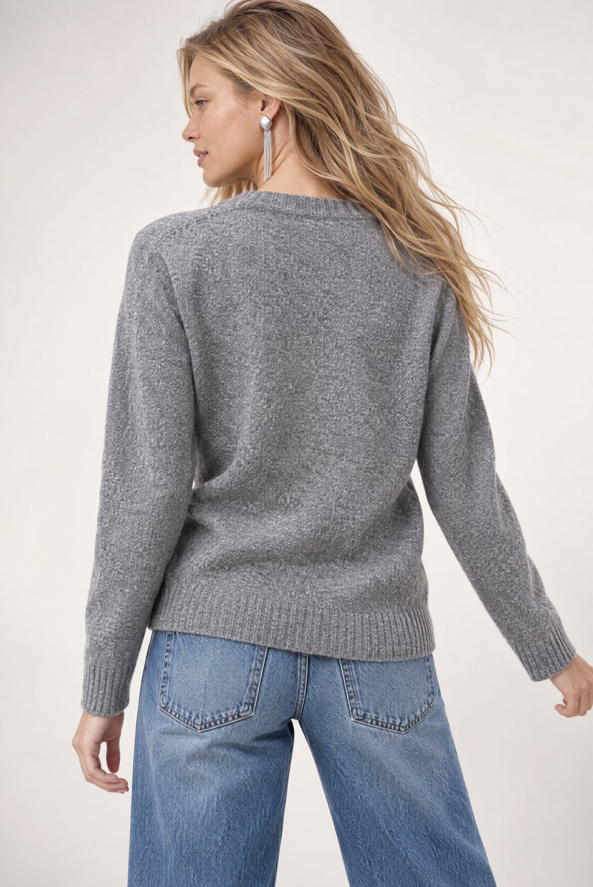 Gray knit cardigan with ribbed trim worn over blue jeans, shown from back view.