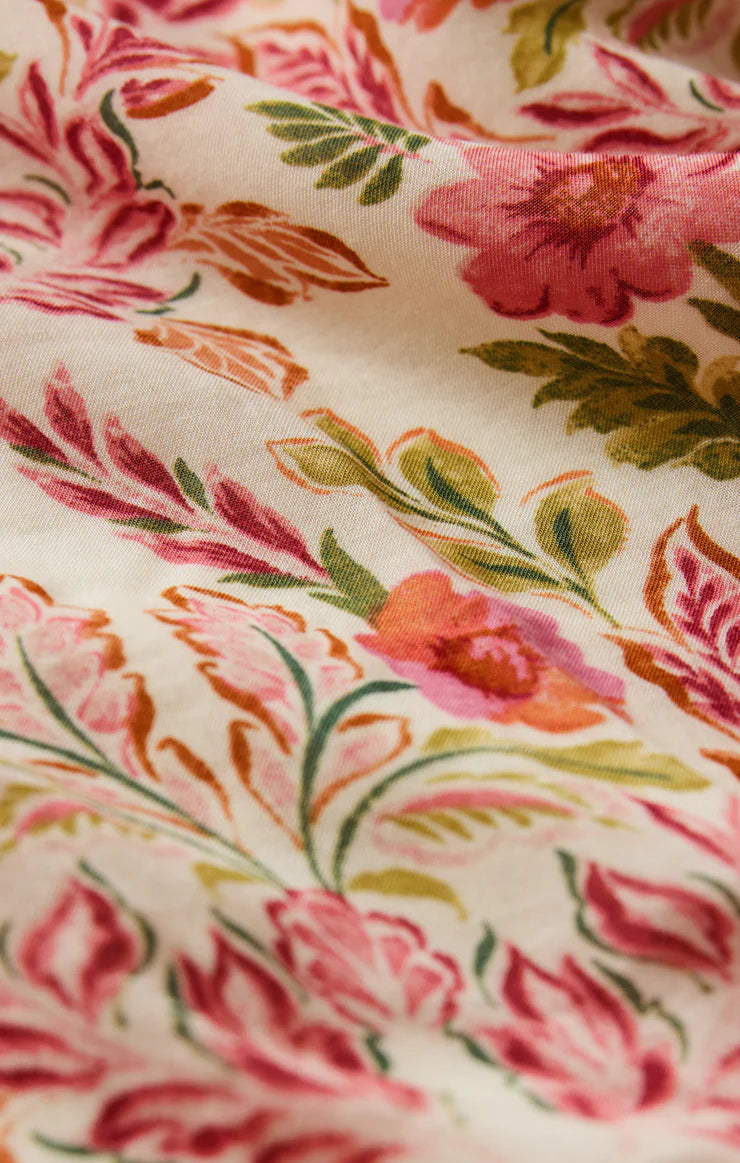 Close-up of the Cornelia Ami Floral Midi Dress by Z Supply, featuring cream-colored fabric with a textured voile feel and a floral pattern in pink, red, green, and orange. Soft material and gentle folds create subtle shadows for an elegant look.