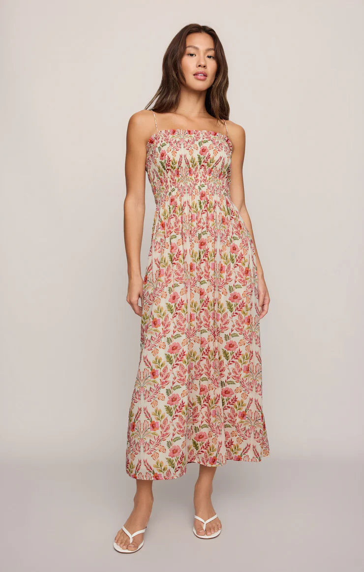 A woman in the Z Supply Cornelia Ami Floral Midi Dress—sleeveless with a square neck and pink and green florals—stands against a plain light background, pairing the textured voile midi dress with white sandals.