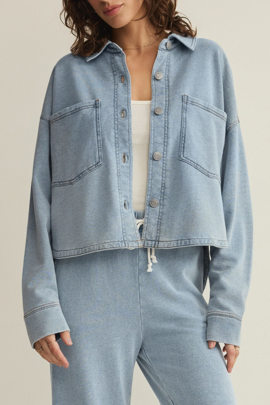 A person wears the Z Supply All Day Cropped Knit Jacket in light blue over a white top, paired with matching light blue pants. Their face is partially out of frame.