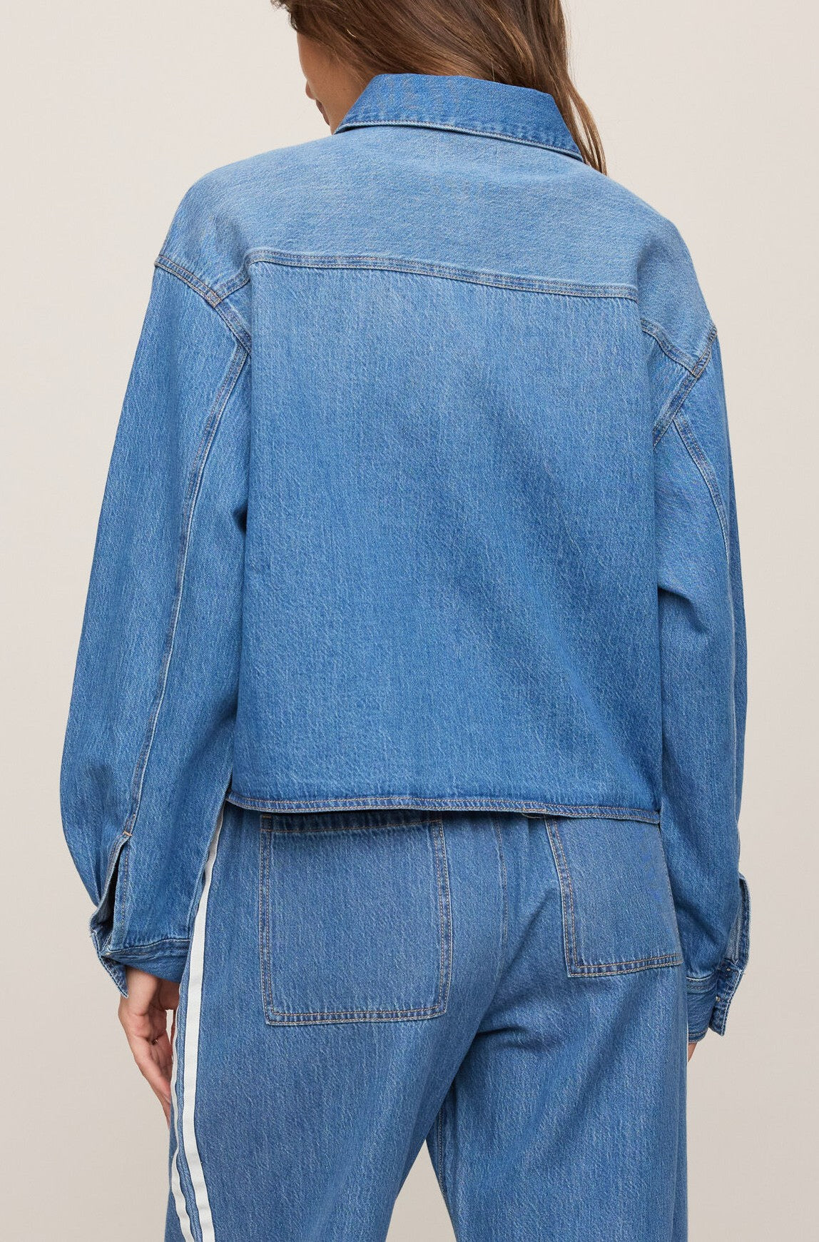 A person, seen from the back against a plain light background, is wearing the Z Supply Erin Denim Jacket—made from 100% cotton blue denim—paired with matching blue denim pants featuring white side stripes.
