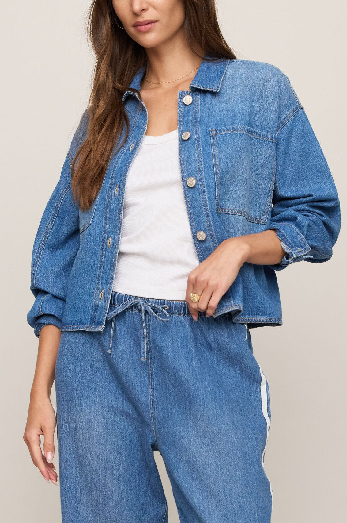 Wearing the Erin Denim Jacket in DREAMSTATE by Z Supply over a 100% cotton white collared shirt and regular fit blue jeans, the woman stands against a neutral background with her hand resting on her waist. Her face is partially visible.