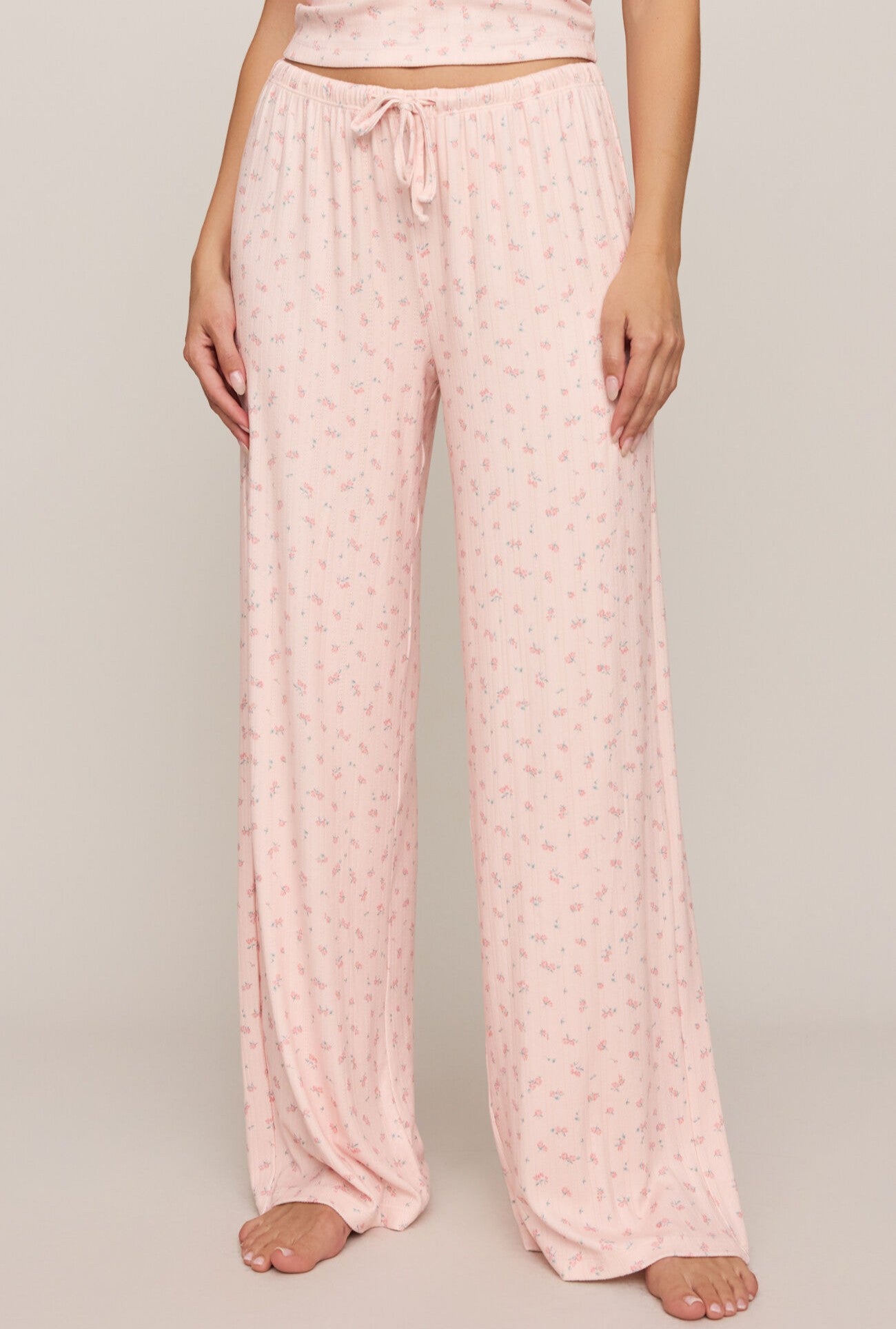 A person wears the Z Supply Better Off Ditsy Pant in Pink Multi, featuring a loose, high-rise fit with a small floral print, wide leg, full length, and a drawstring waistband, standing barefoot against a plain background.