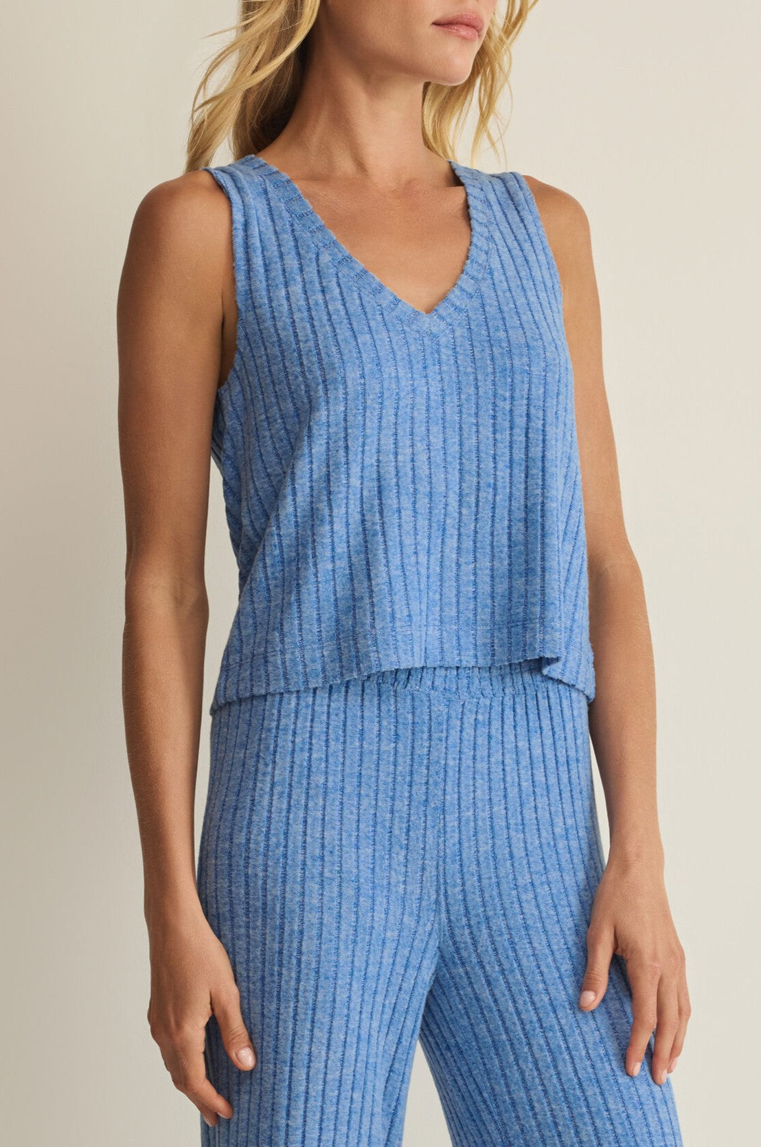 A woman wears the Sloane V Neck Rib Tank by Z Supply with matching ribbed pants, posing against a neutral background. Her blonde hair is loose and her arms rest gently by her sides.