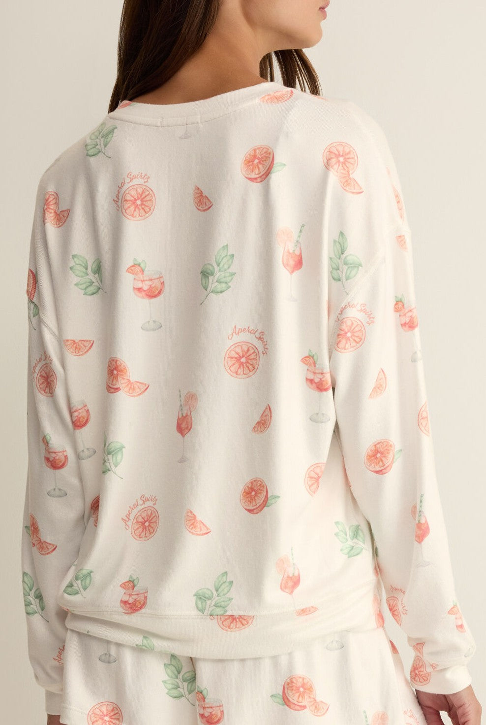 A woman is seen from the back wearing the Z Supply Spritz Pj Top, a silky jersey pajama top featuring a spritz print with pink grapefruit, green leaves, and cocktail designs; matching relaxed-fit shorts are partially visible.