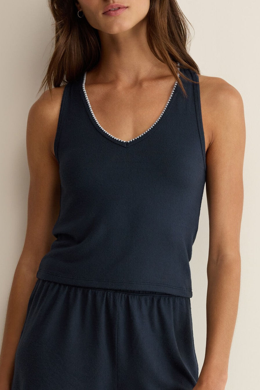 A woman models the Z Supply Stately V-neck Tank in navy, featuring a sleeveless cut and white trim, paired with matching bottoms. Her face is partially out of frame against a neutral background—a sophisticated wardrobe staple.