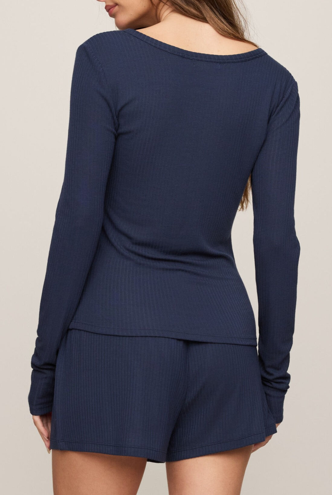A woman with long hair is seen from the back, wearing the Z Supply Just Right Rib Long Sleeve Top in navy blue, featuring a button front and a comfy fit, making it ideal for casual lounging.