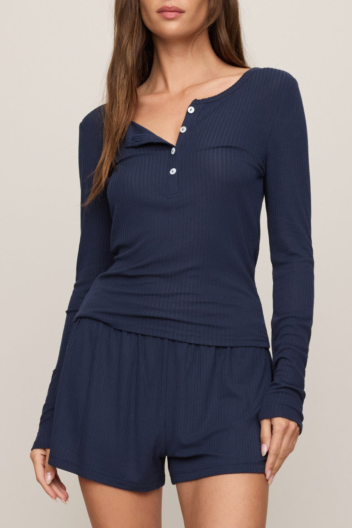 A woman wears the Z Supply Just Right Rib Long Sleeve Top in navy, featuring a cozy ribbed texture and button front, paired with matching shorts. Ideal for loungewear or sleepwear, her face is partially out of frame.