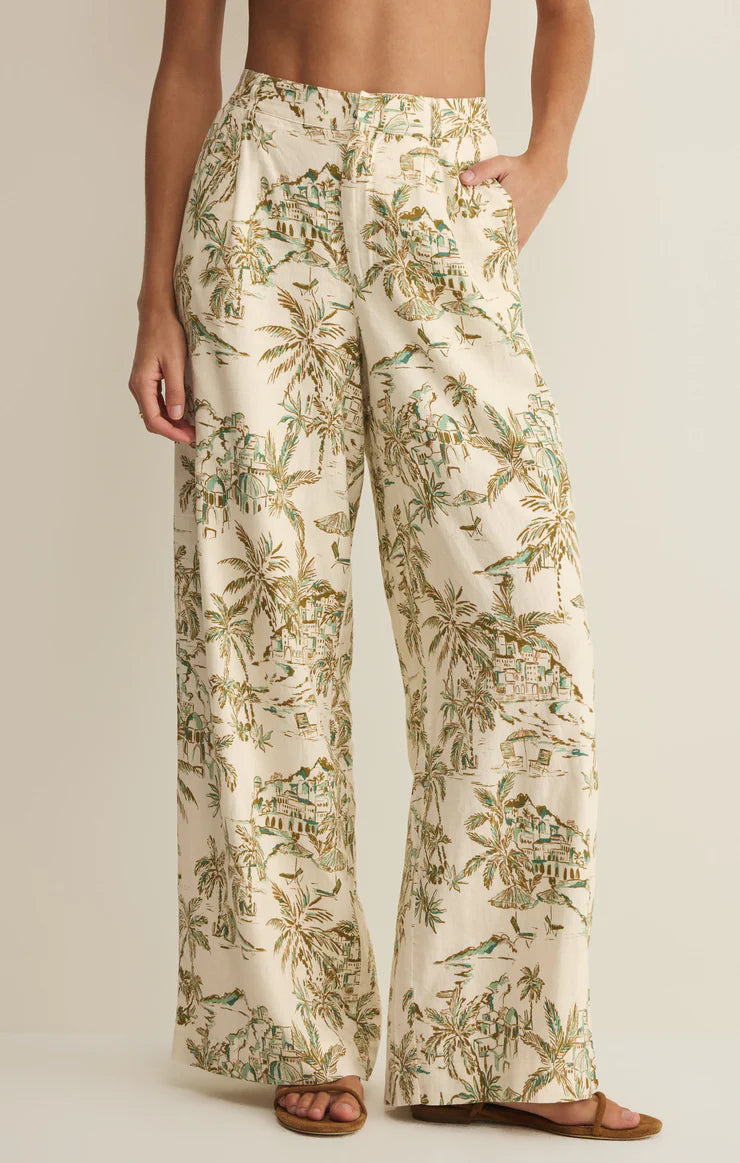 A person wears Z Supply's Overlook Tiki Tide Linen Pant in Cream Multi, featuring a tropical print and wide leg high-rise fit, paired with brown sandals. Their top is not visible in the image.