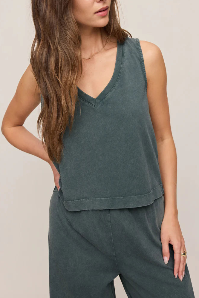 A woman with long brown hair models the Z Supply Sloane V-neck Top in Emerald Cove, paired with matching pants. She stands with one hand on her hip against a plain light background, her face partially out of frame.