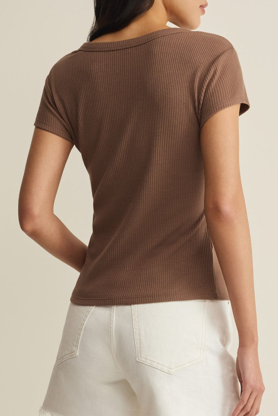 A person is seen from behind, wearing the Z Supply Leisurely Tee in brown with high-waisted white denim shorts against a plain light background.
