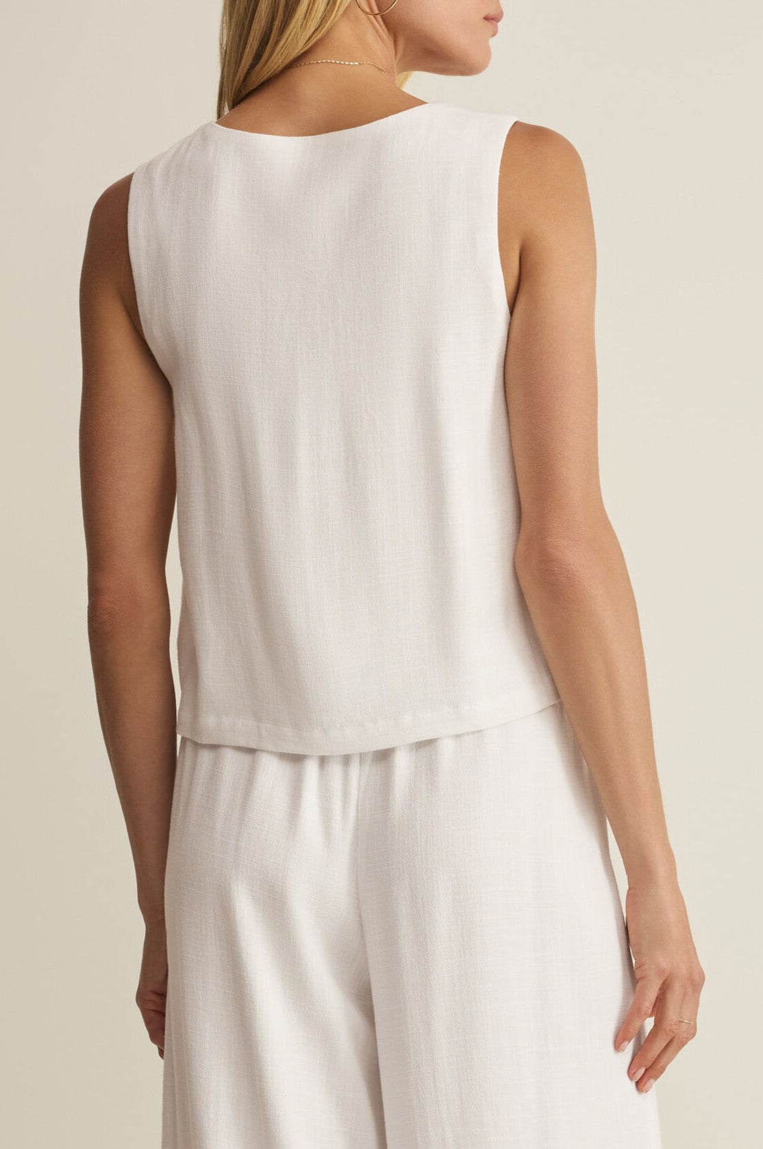 A woman is shown from the back wearing the Z Supply Charli Top, a regular fit, square neck sleeveless white top paired with matching loose white pants, standing against a plain light background.