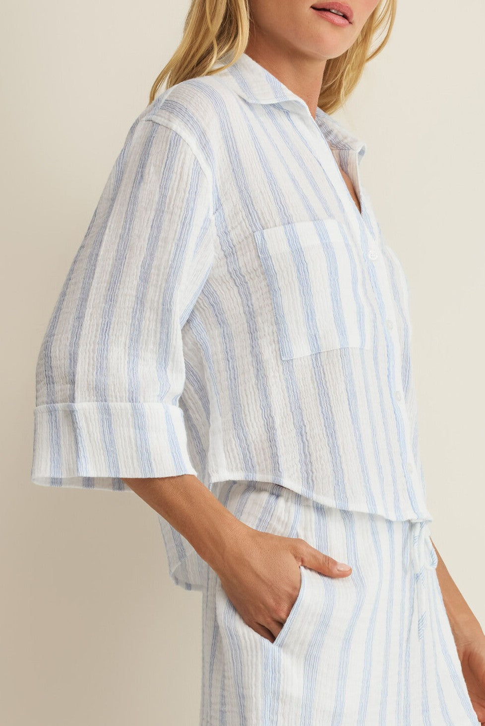 A woman wears the Helena Striped Shirt by Z Supply, a textured cotton blouse with three-quarter sleeves and stripe print, paired with matching pants and one hand in her pocket.