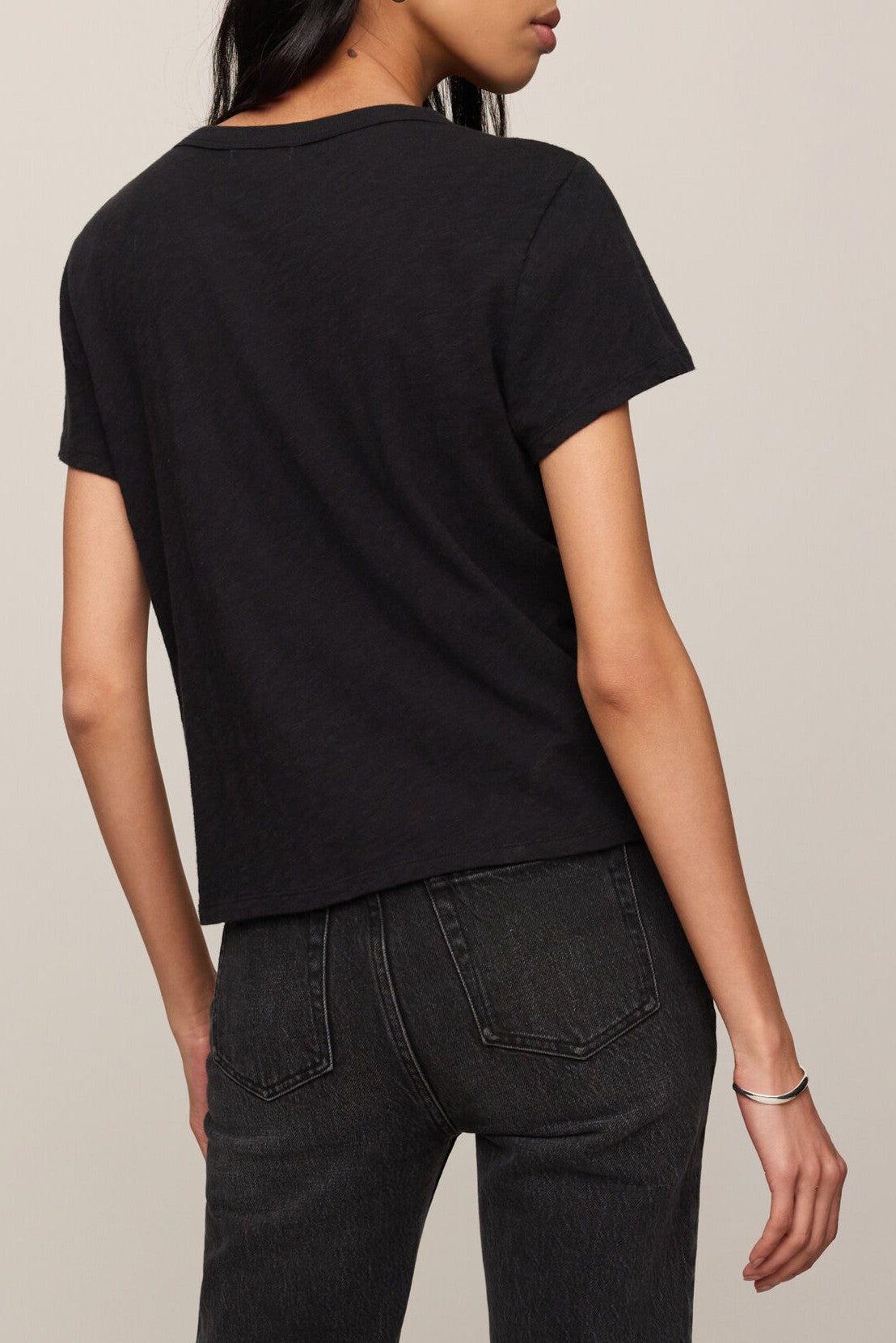A person with long dark hair is seen from behind, posing against a neutral background while wearing the Z Supply Junie Slib Tee Shirt—a black, regular fit crew neck top crafted from 100% cotton—paired with dark jeans.