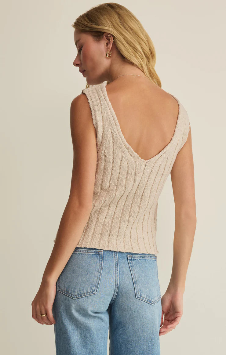 A woman with long blonde hair models the Z Supply Acadia Sweater Tank—a sleeveless, light beige ribbed knit top with a deep V-back—paired with light blue jeans against a plain background.