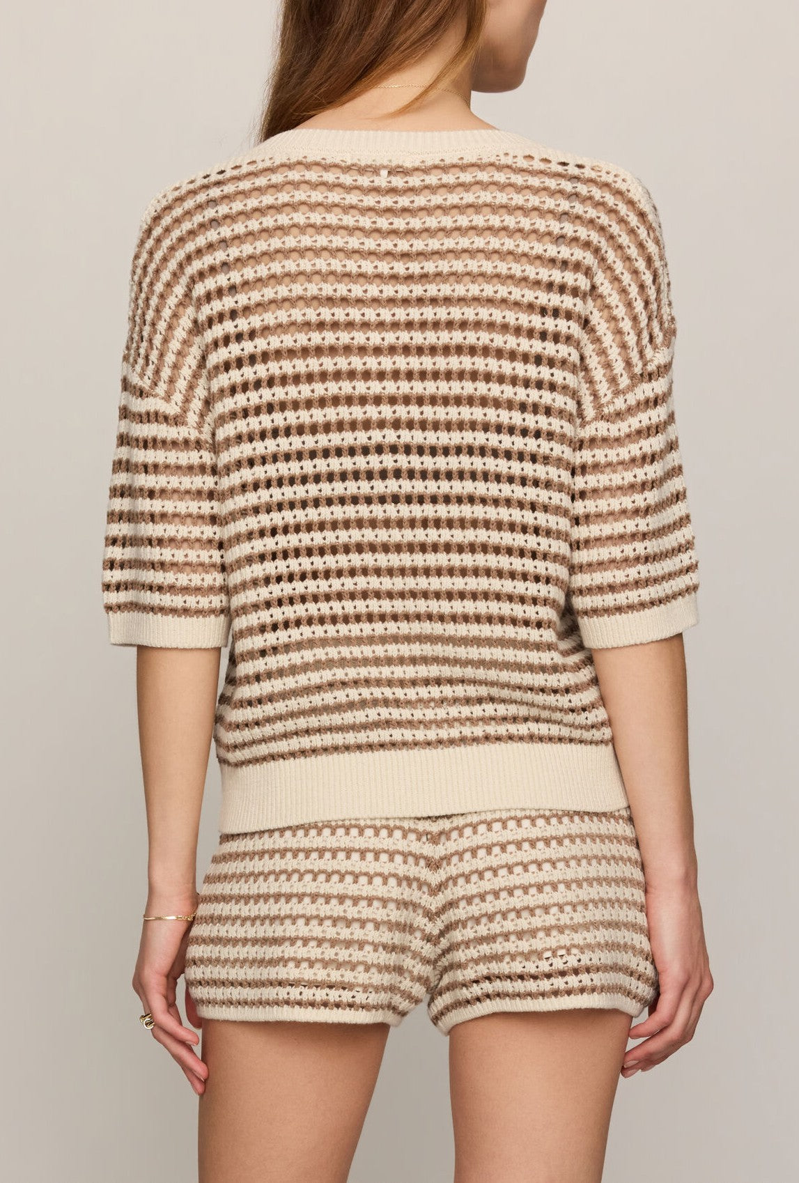 A woman is seen from the back wearing Z Supply's Kylo Striped Polo Sweater in beige and cream, featuring a cotton-viscose crochet knit, short sleeves, and a relaxed fit with matching high-waisted shorts for a casual look.