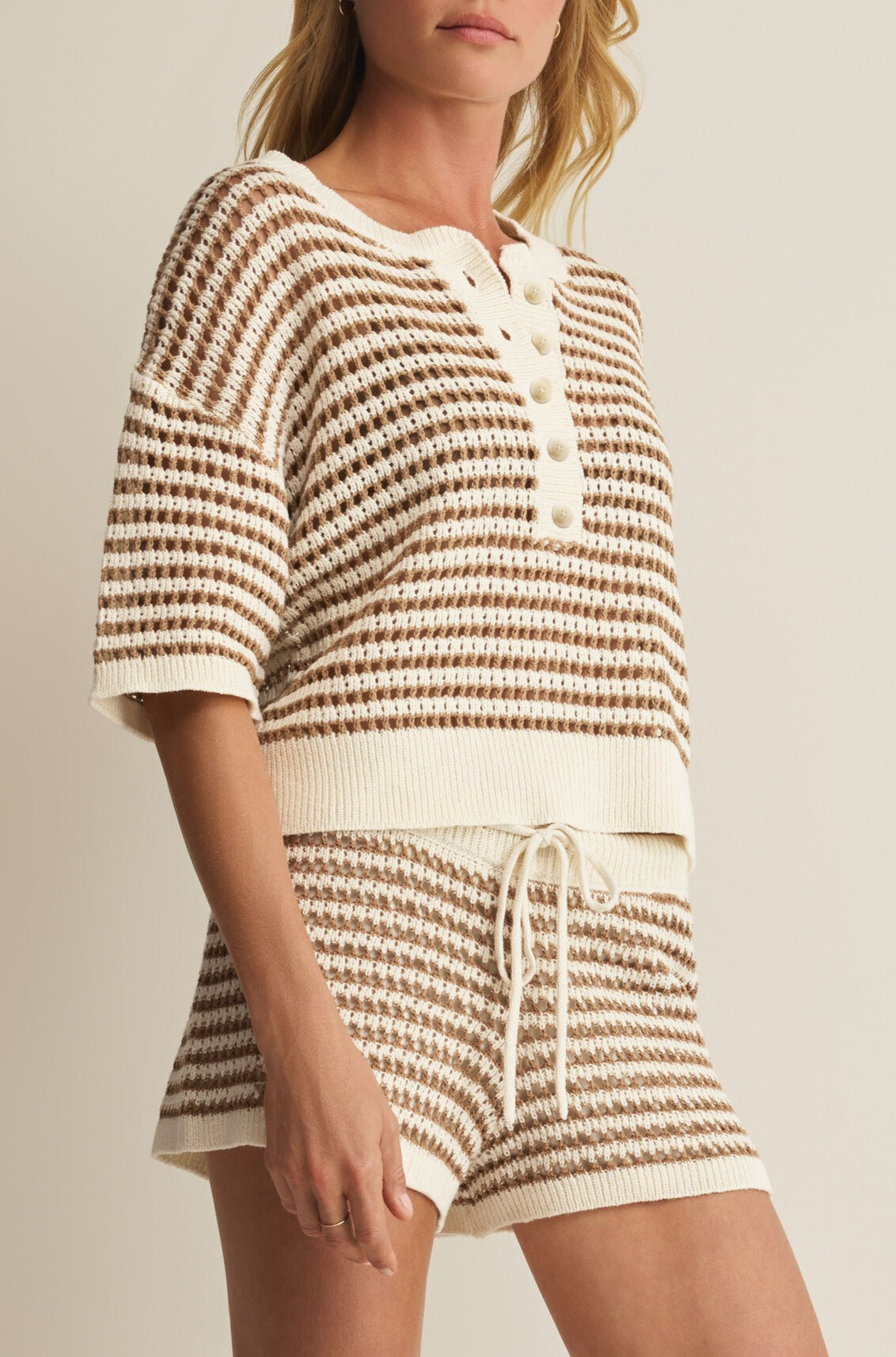 A woman wears the Kylo Striped Polo Sweater by Z Supply, a casual cream and brown striped short sleeve top with a buttoned neckline, crafted from soft cotton viscose.