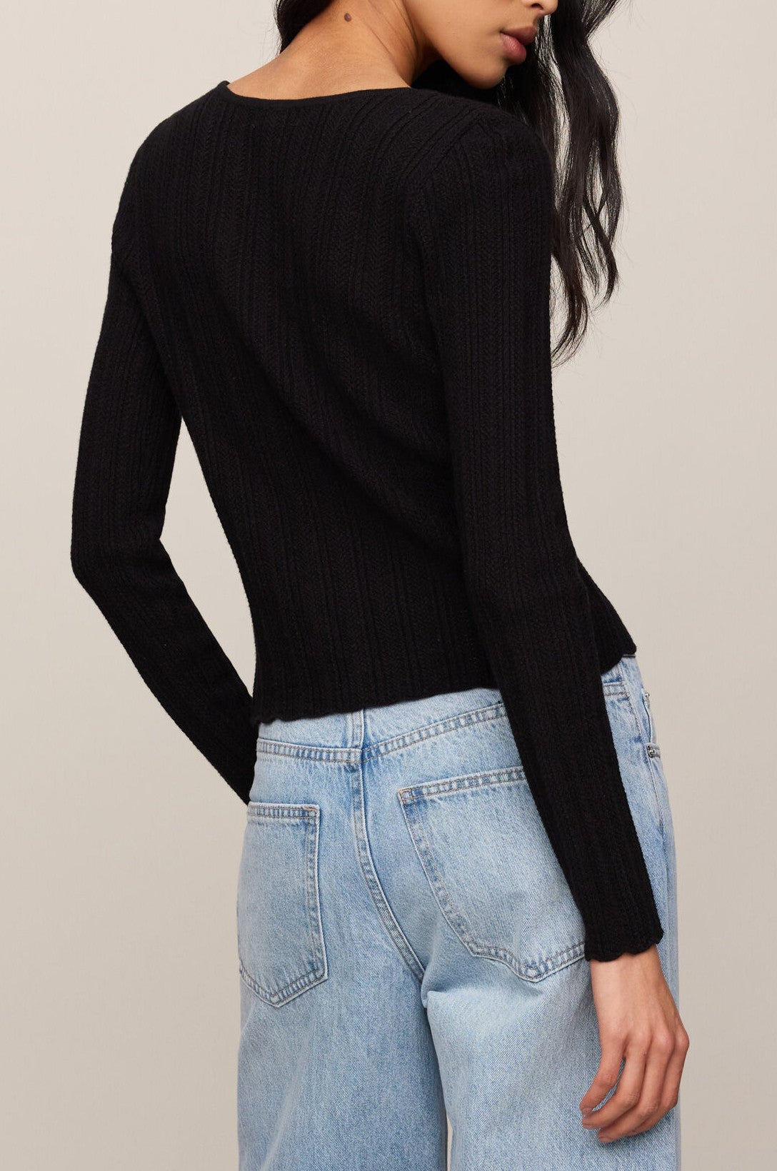 A person with long dark hair is shown from the back against a neutral background, wearing the Z Supply Landa Sweater Top in black ribbed fabric and light blue high-waisted jeans.