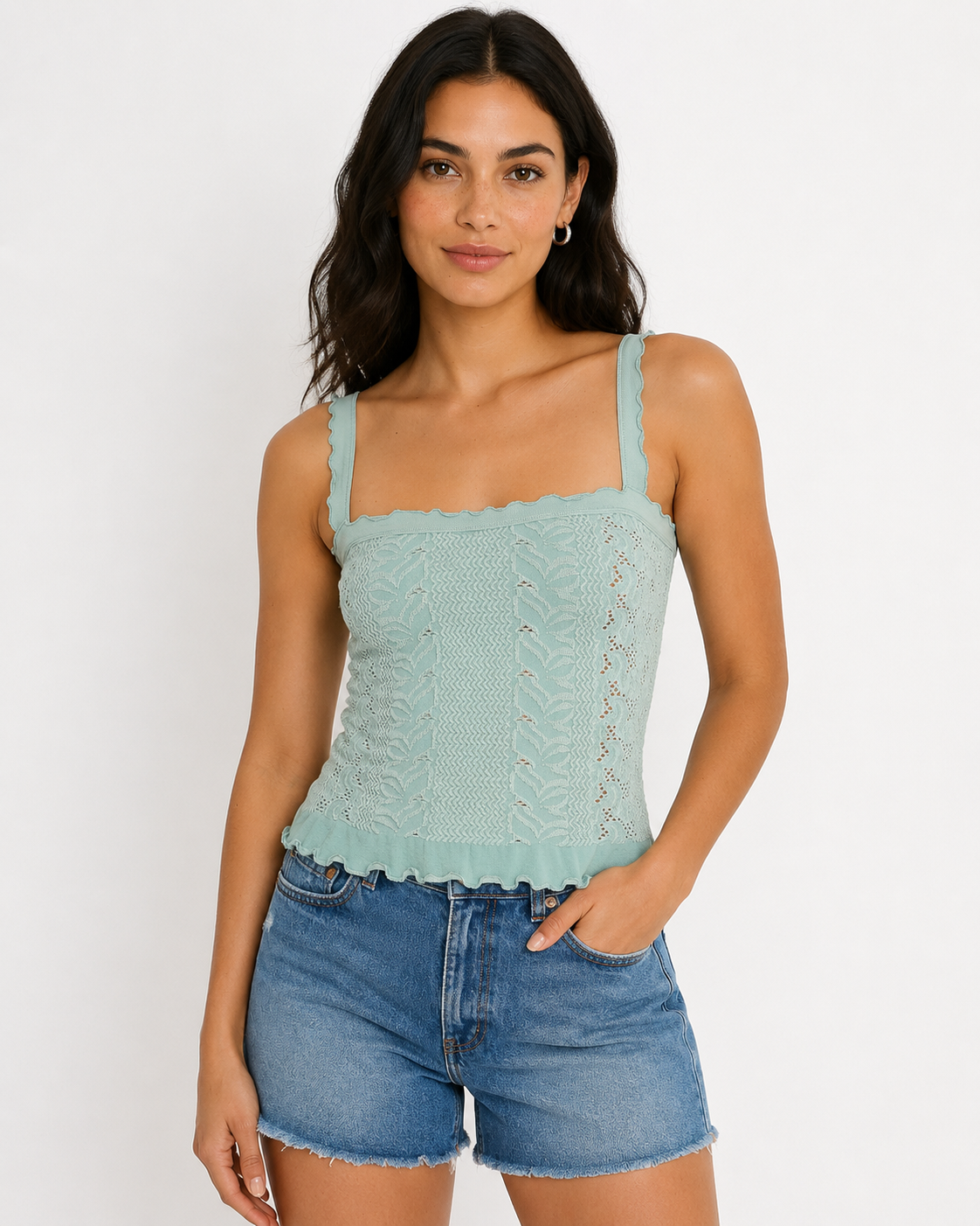 A woman with long wavy hair stands against a white background wearing the Free People So Soft Femme Square Top and blue denim shorts. She styles the look with minimal jewelry and her left hand in her pocket.