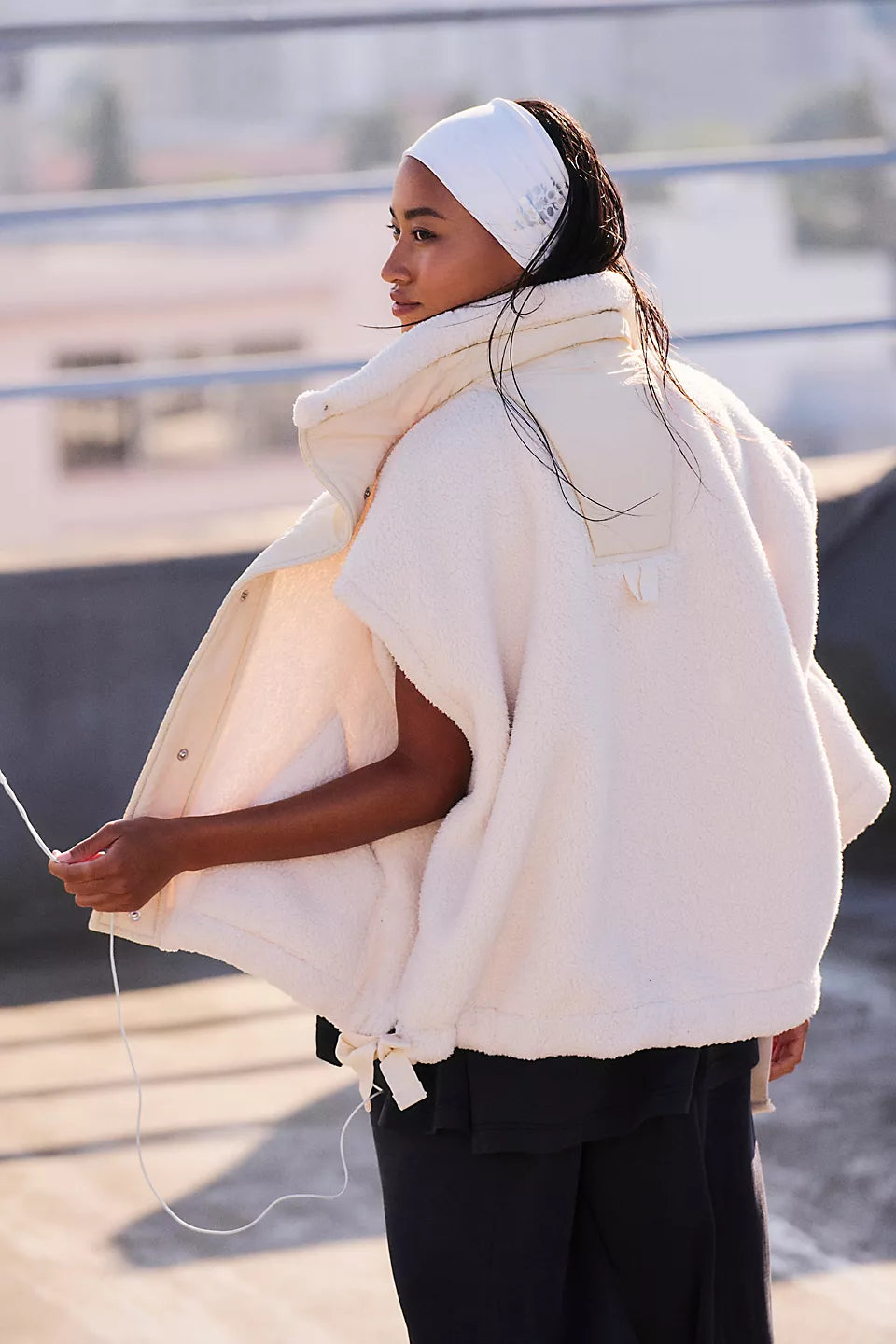 Cream-colored puffer vest with large collar worn over black pants, shown from behind.