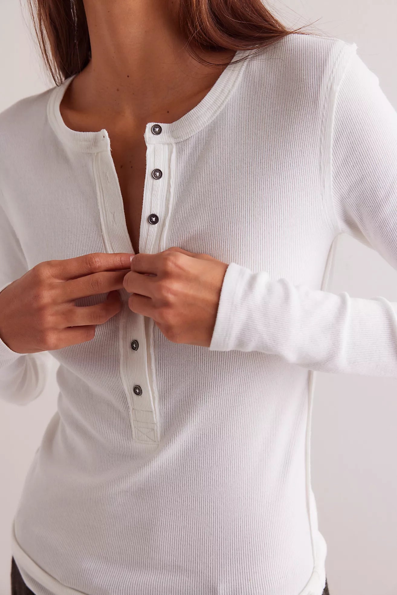 A person is fastening the buttons on the Jamie Henley in Ivory by Free People, a white, cotton long-sleeve, button-up shirt. The photo is cropped to show only their torso and hands.