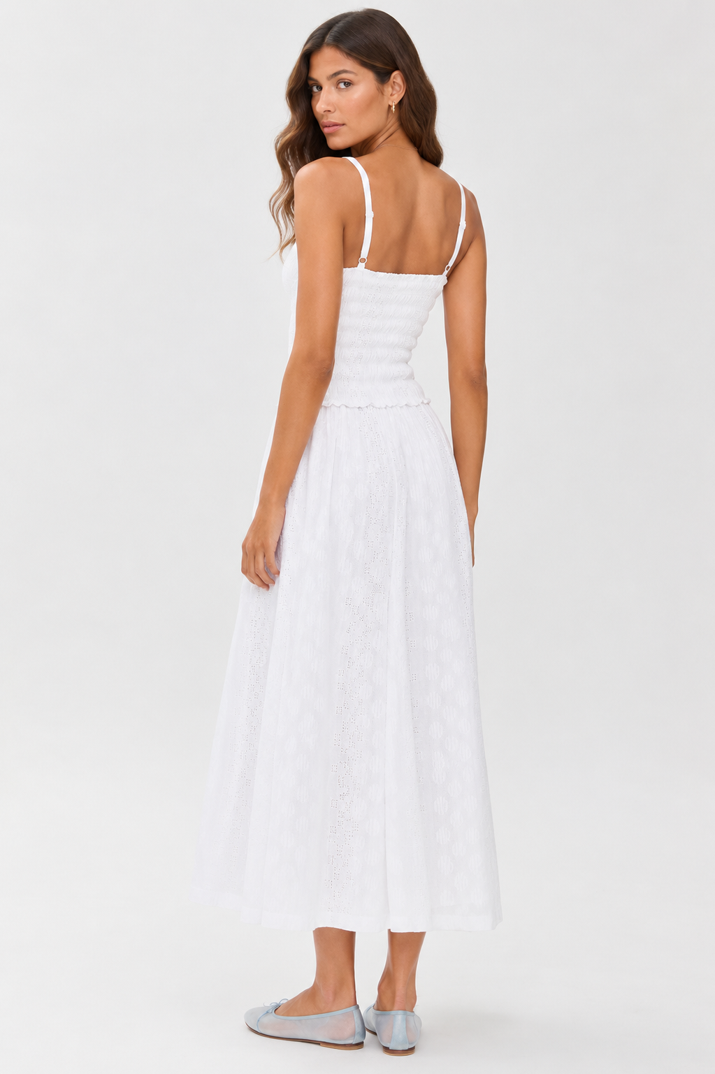 Woman with long wavy brown hair stands sideways, looking over her shoulder, wearing the Splendid Kendra Geo Eyelet Dress—a white sleeveless, ankle-length dress with a fitted bodice and flared skirt—paired with light blue flats.