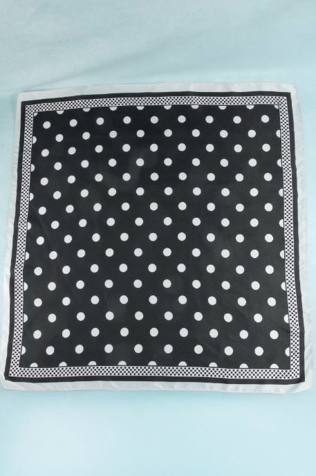 The South Moon Under Polka Dot Scarf, featuring a black satin finish with white polka dots and a crisp white border, is laid flat on a light blue background.