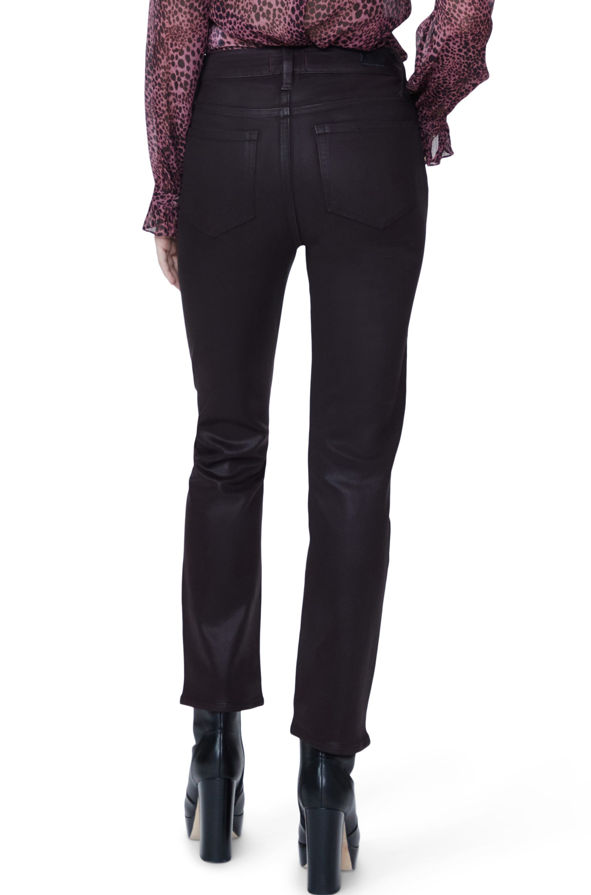 A person is seen from the back against a white background, wearing Paige’s Cindy Jean in Black Cherry, paired with a long-sleeve pink patterned blouse and black heeled boots.