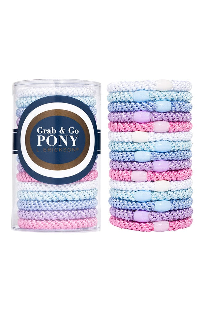 A clear Grab & Go Pony Tube (15 Ponies) by The Finest Accessories, filled with multi-colored hair ties, sits beside a stack of the same pastel pink, purple, and blue hair ties.