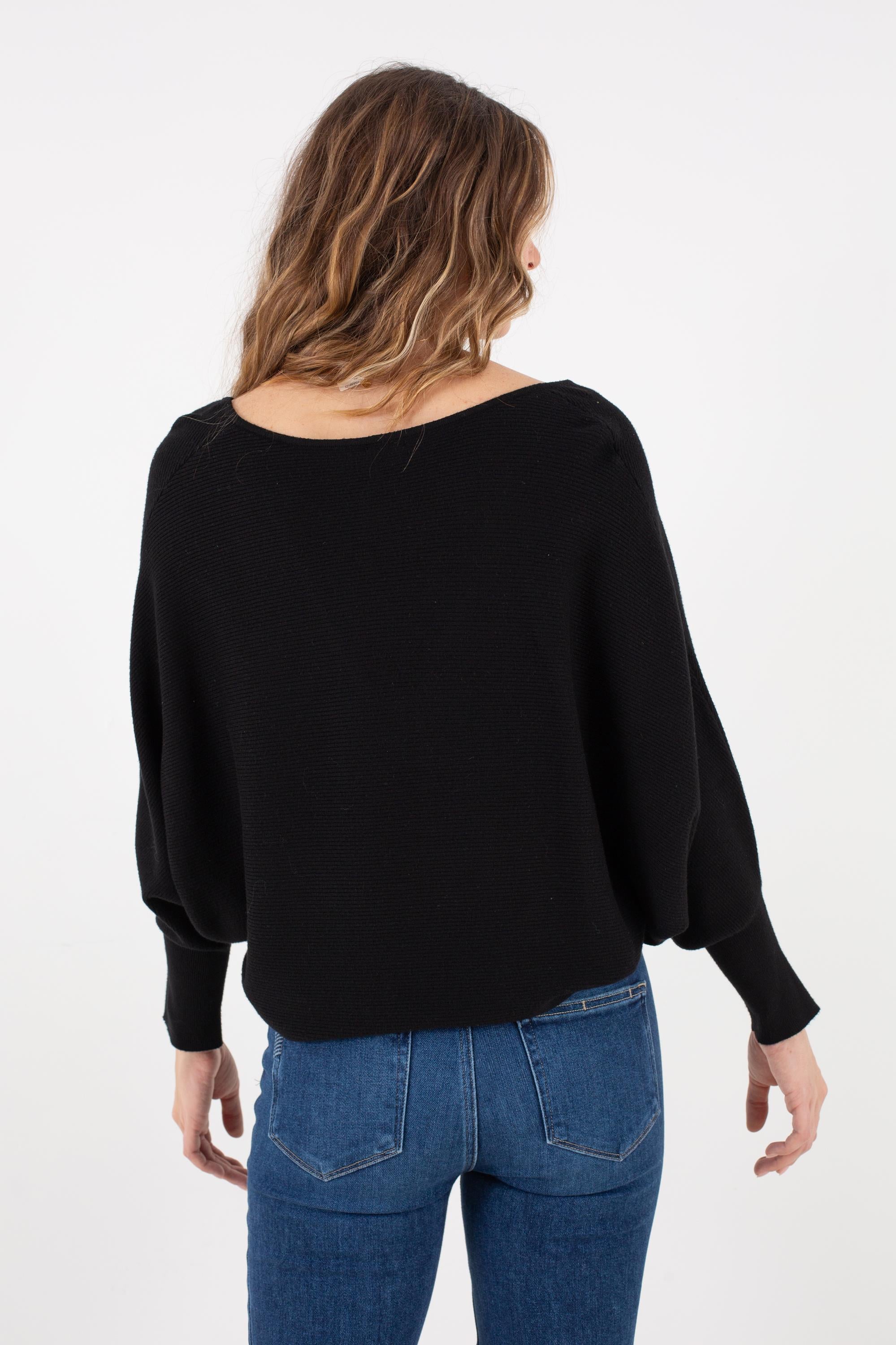 A person with wavy hair, wearing the Kerisma Dolman Ryu V Neck in black and blue jeans, is facing away from the camera against a plain white background.