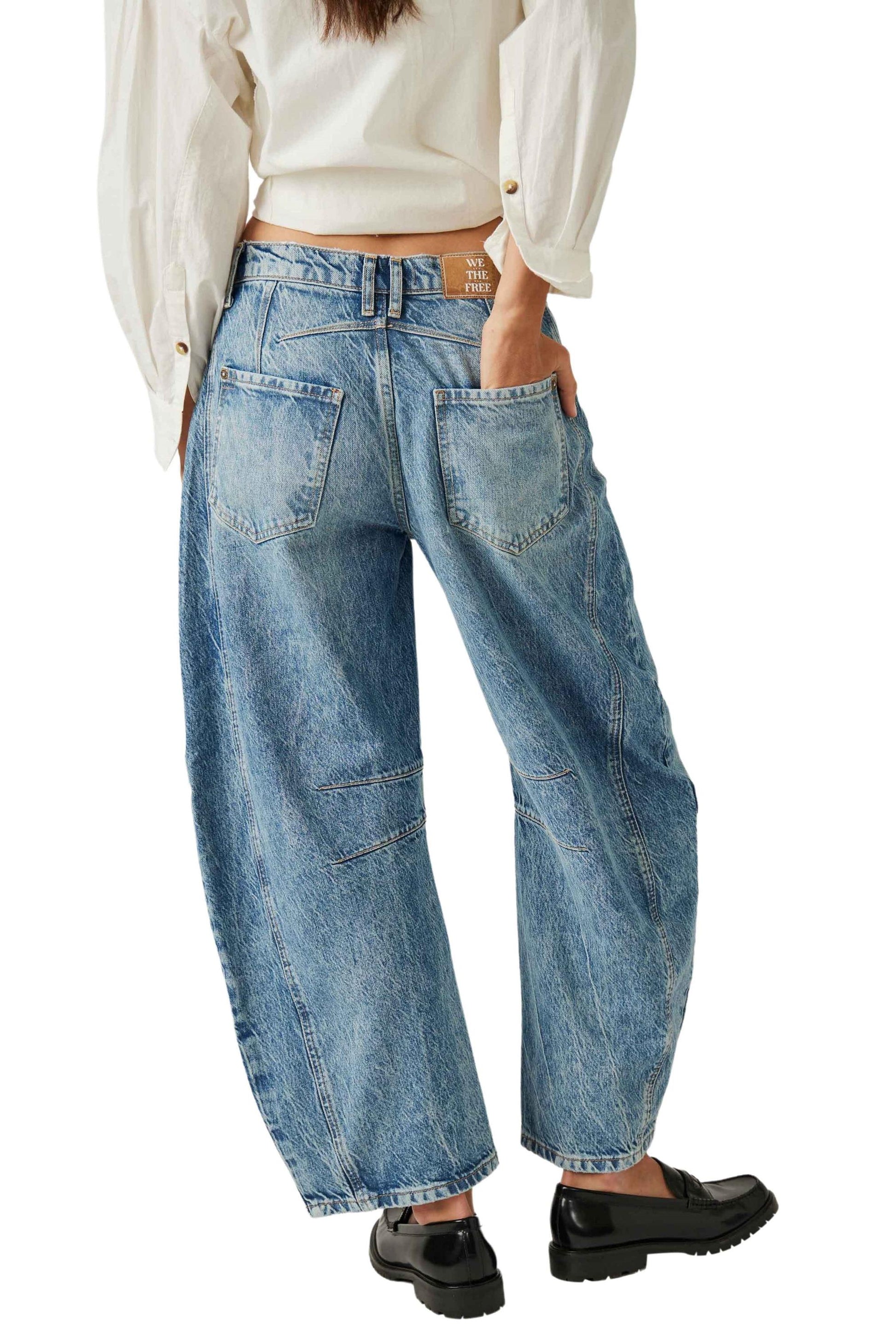 A person shown from the back wears a white long-sleeve shirt, blue Good Luck Mid Rise Barrel jeans by Free People with five pockets including back pockets, and black loafers.