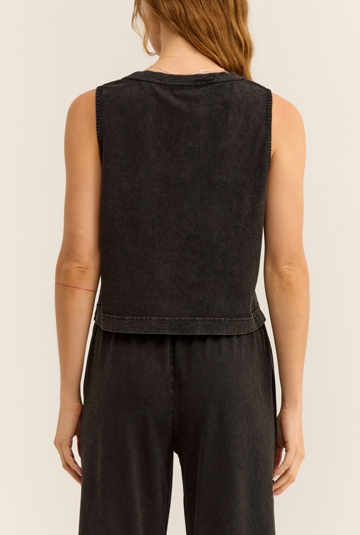 A person with long, light brown hair is photographed from the back against a neutral background, wearing the Z Supply Sloane V-neck Top in Black paired with matching black pants.