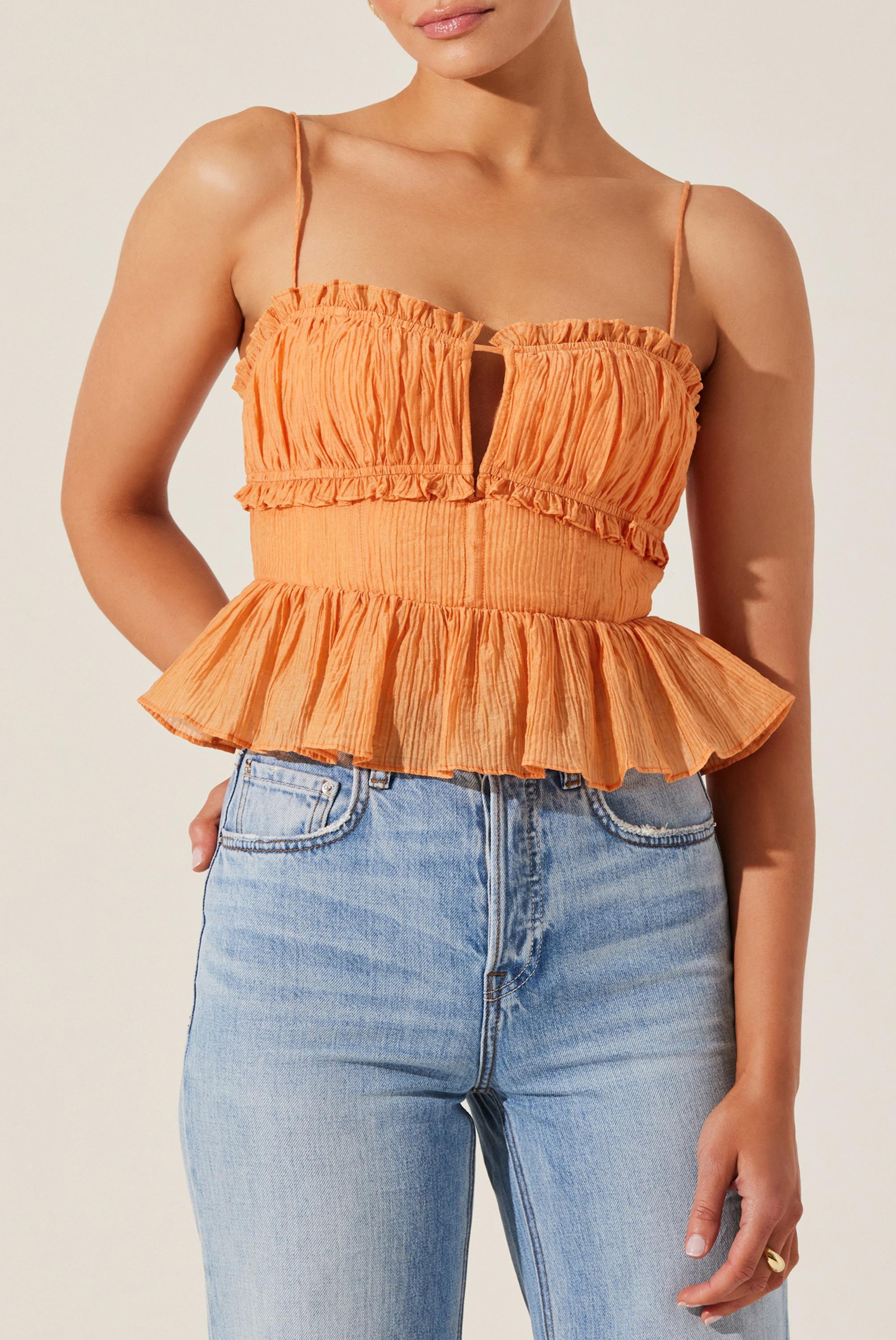 A woman wearing the ASTR Sylvan Top in PAPAYA—a light orange, sleeveless peplum top with ruffle trim and spaghetti straps—paired with high-waisted light blue jeans, shown from shoulders to hips.