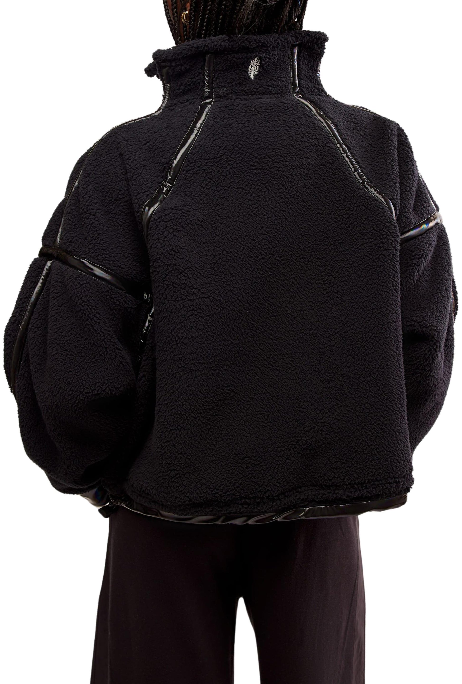 A person is seen from behind wearing the FP Movement Mountain High Shine 1/2 Zip, a loose black fleece jacket with shiny trim, high collar, and soft textured look; only their upper body and part of their pants are visible.